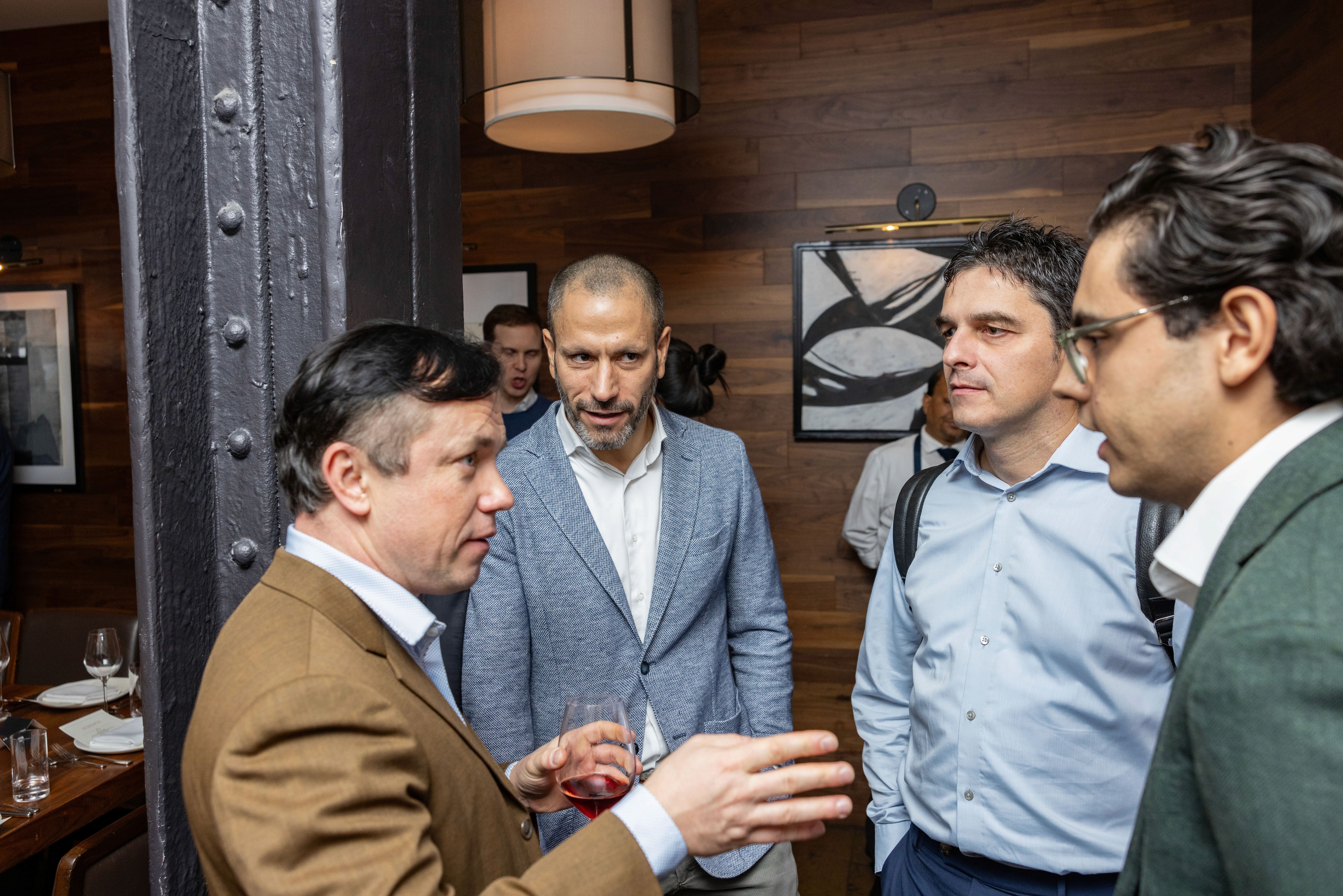 Four men engage in a conversation, with one gesturing animatedly in a stylish interior space.
