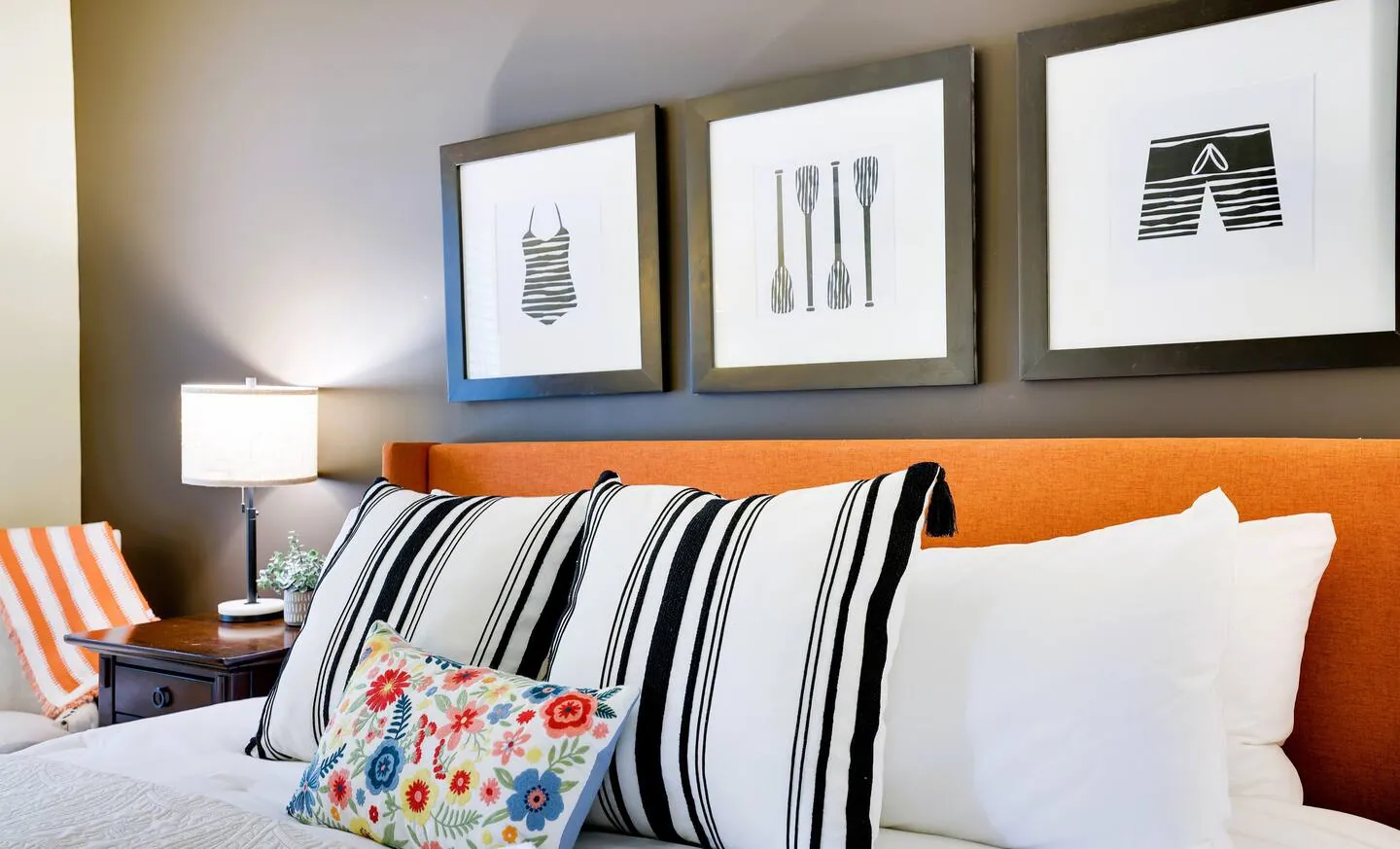 King bed with striped and floral pillows under three framed prints at Pop's Place