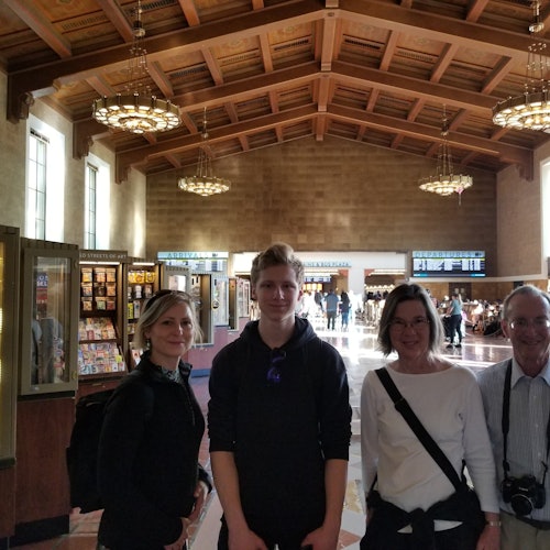 Four people stand inside a spacious hall with high wooden ceilings and hanging chandeliers.