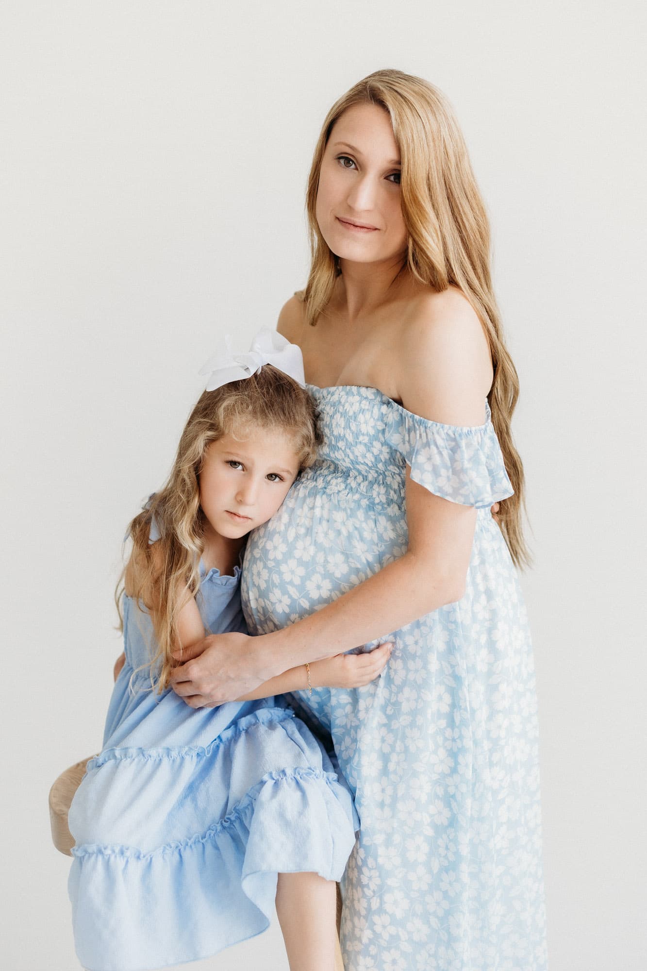 A pregnant mother holds her young daughter close in a soft, natural light setting at Revelator Studio, highlighting the beauty of family photography in Shreveport.