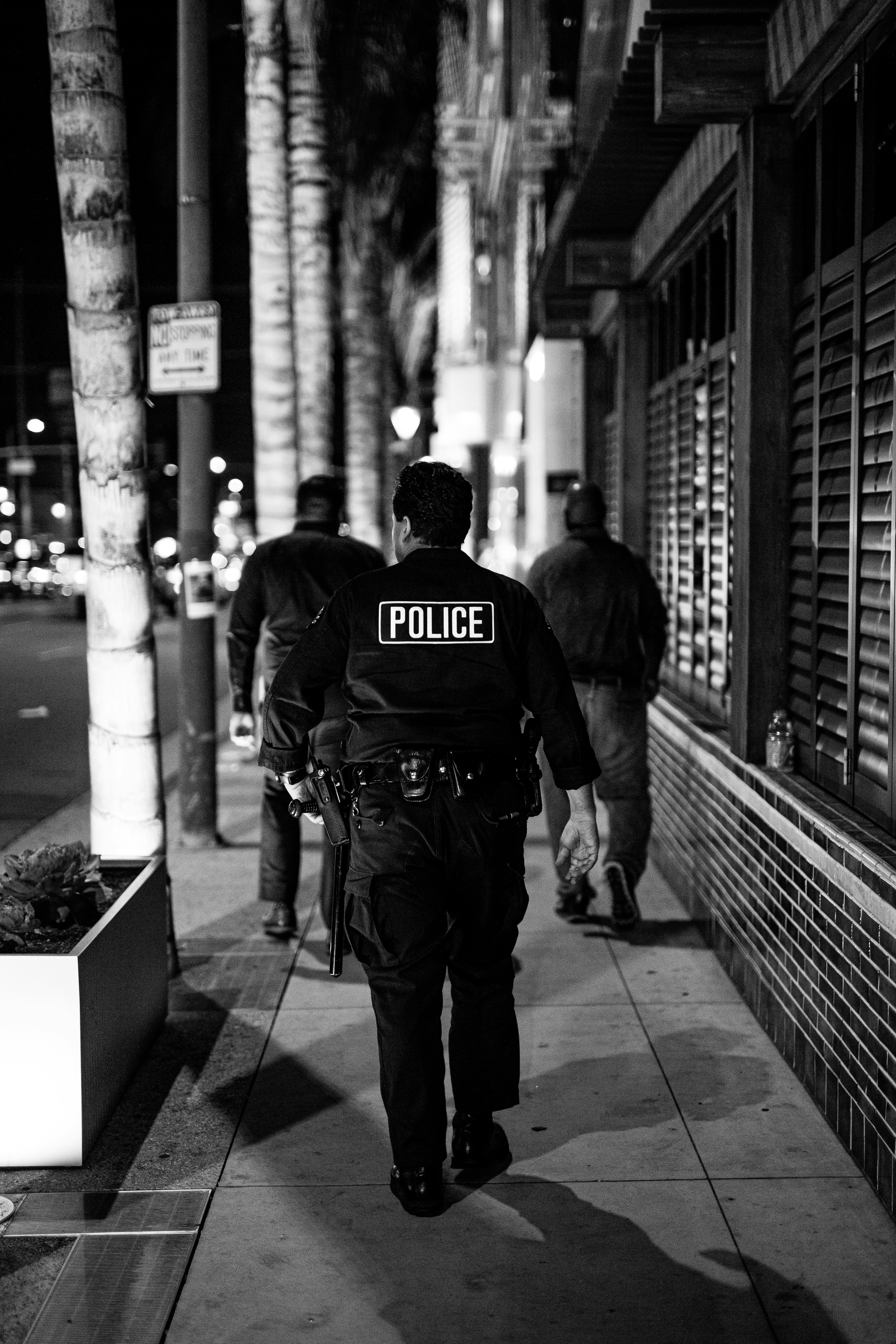 grayscale photo of man in black jacket and pants walking on sidewalk