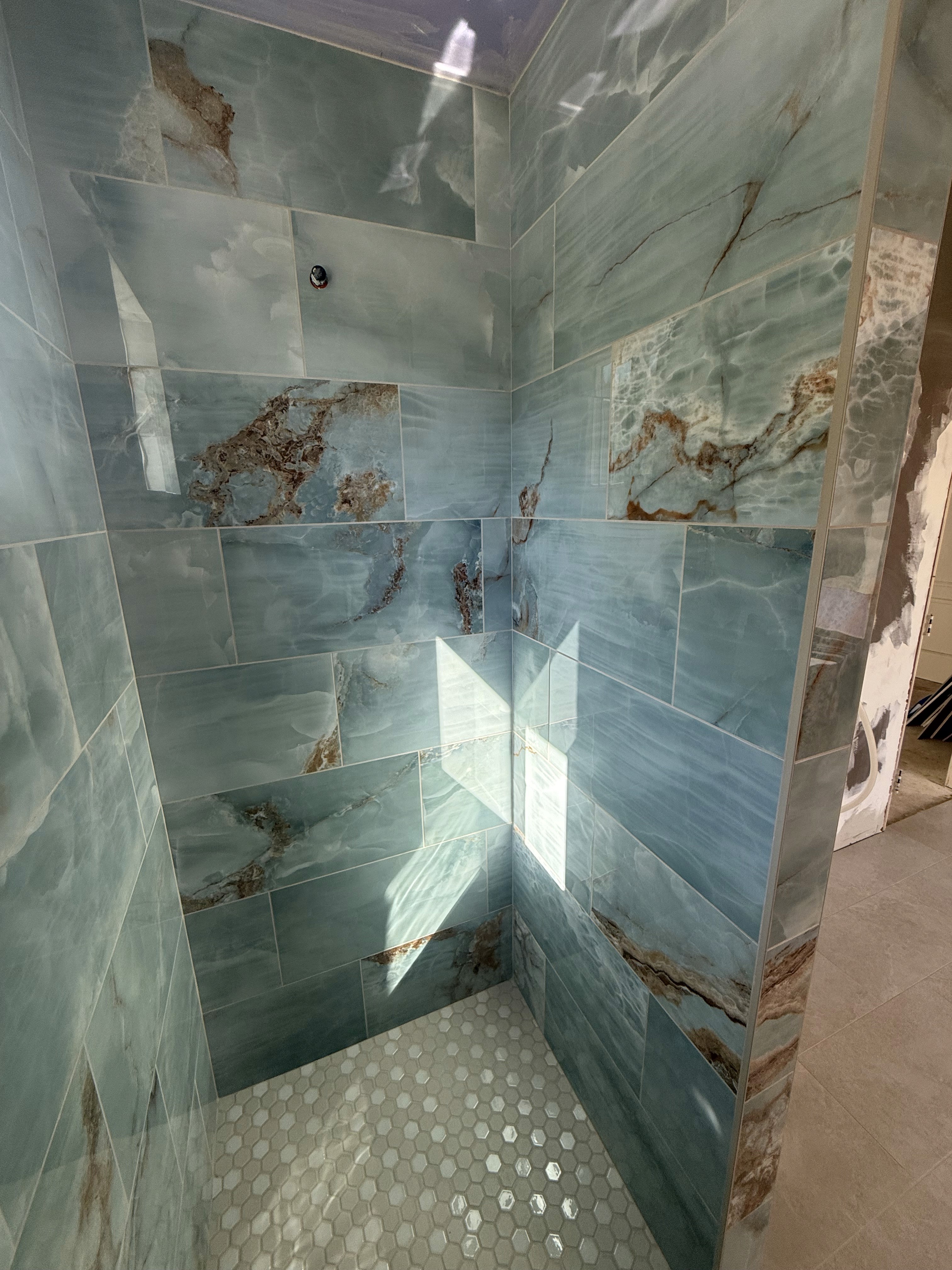 Bathtub shower combo with sleek grey marble-look large format wall tiles, a built-in shower niche with a white and grey hexagonal mosaic tile accent, and modern chrome fixtures.