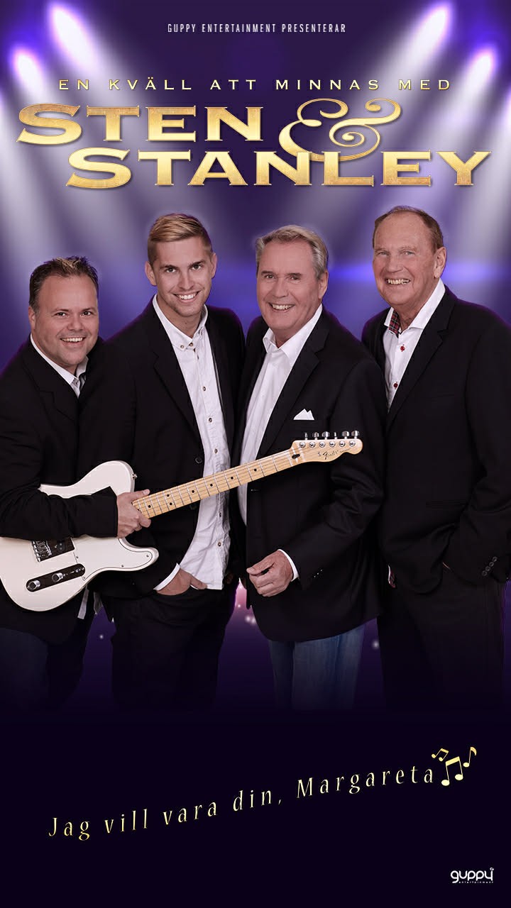 A young person with curly hair smiles at the camera while sitting in front of a laptop against a dark background.