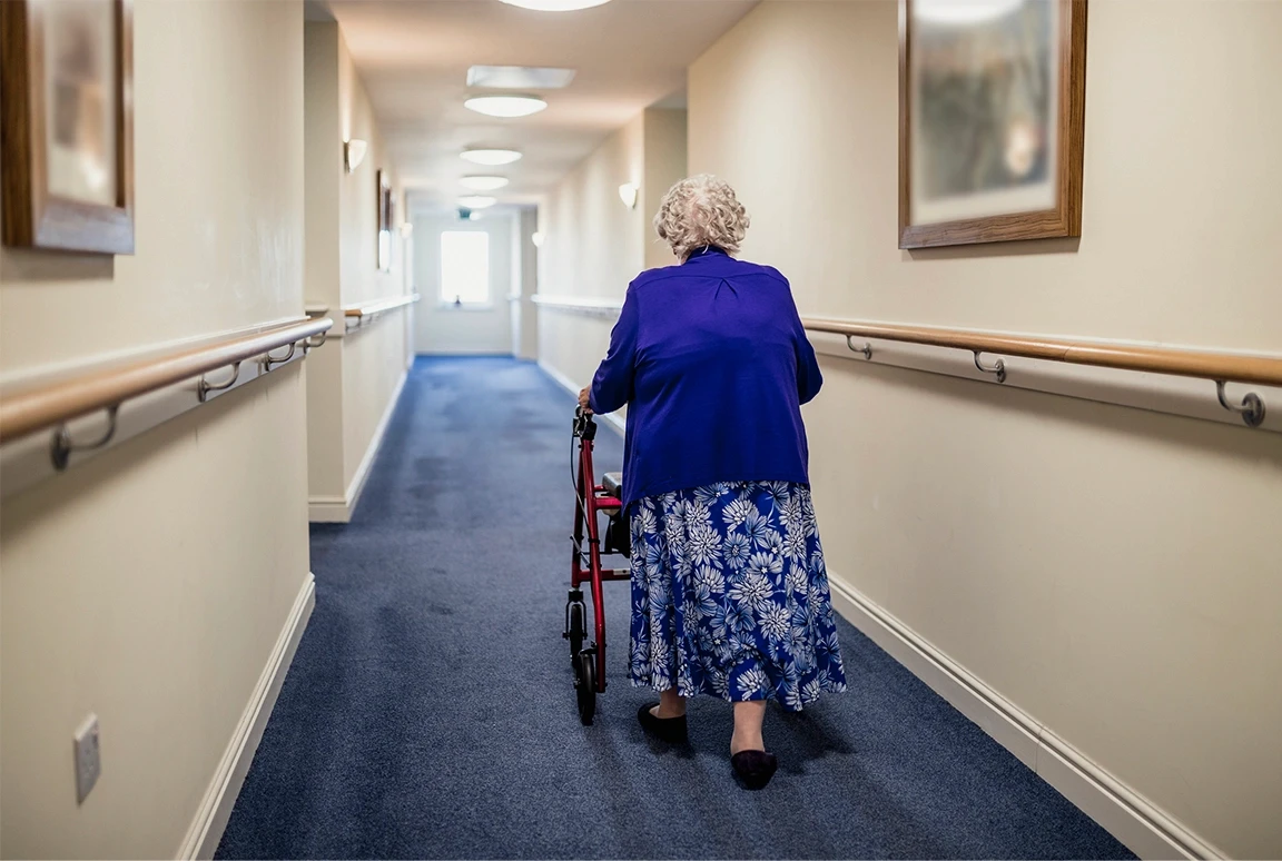 Elderly woman using a walker in an assisted living hallway, symbolizing vulnerability and the need for protection from nursing home abuse