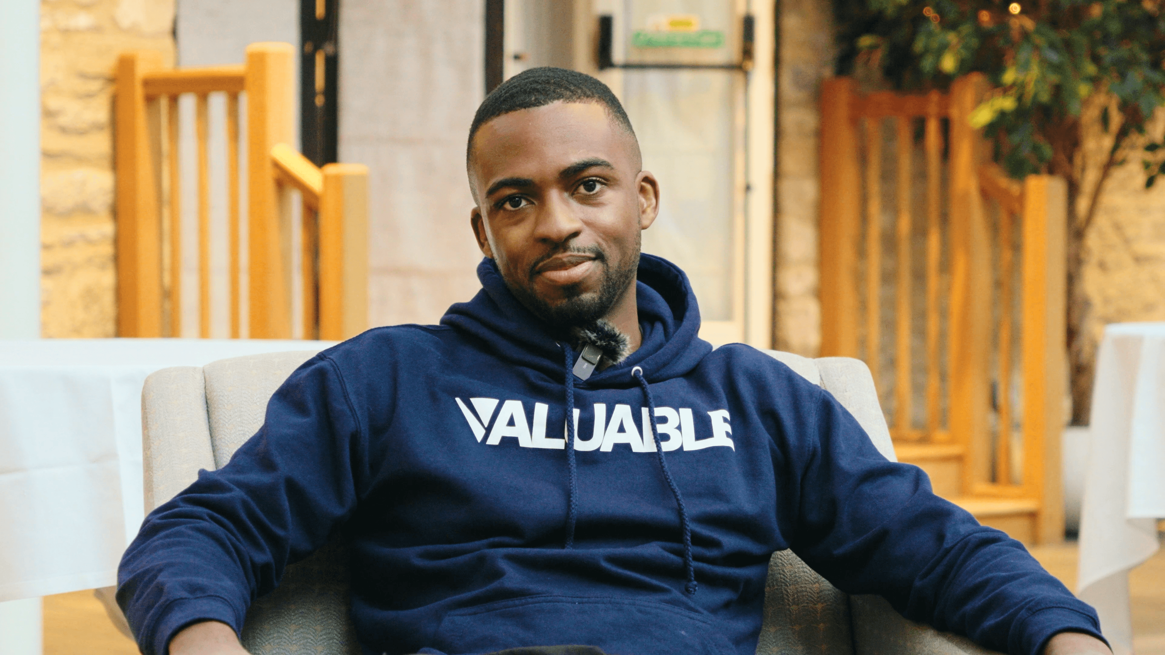 Man in a navy blue valuable hoodie with the word VALUABLE printed on it smiles.
