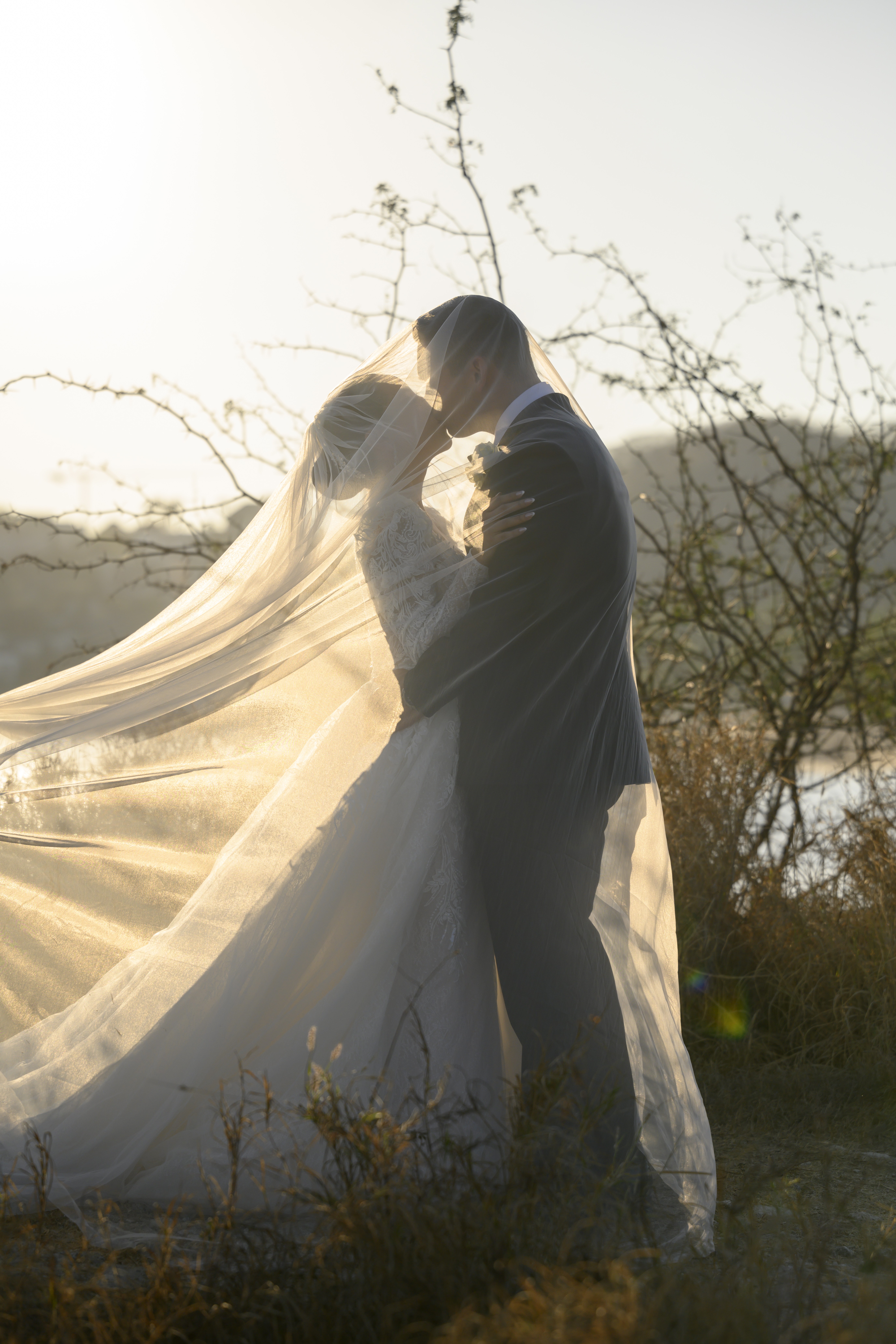 Los novios tomados de la mano, caminando hacia el atardecer en un campo entre las montañas.