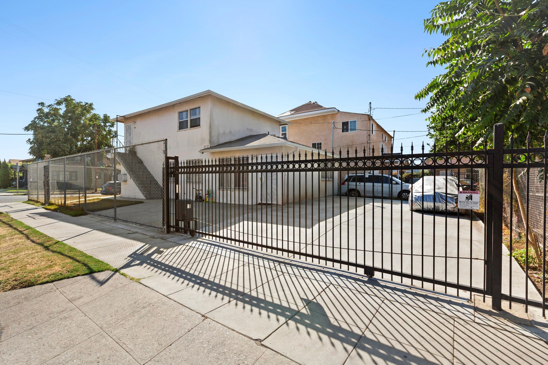 A driveway at 4421 wall, leads to a fenced property with a two-story house under a clear blue sky. Trees line the entrance.