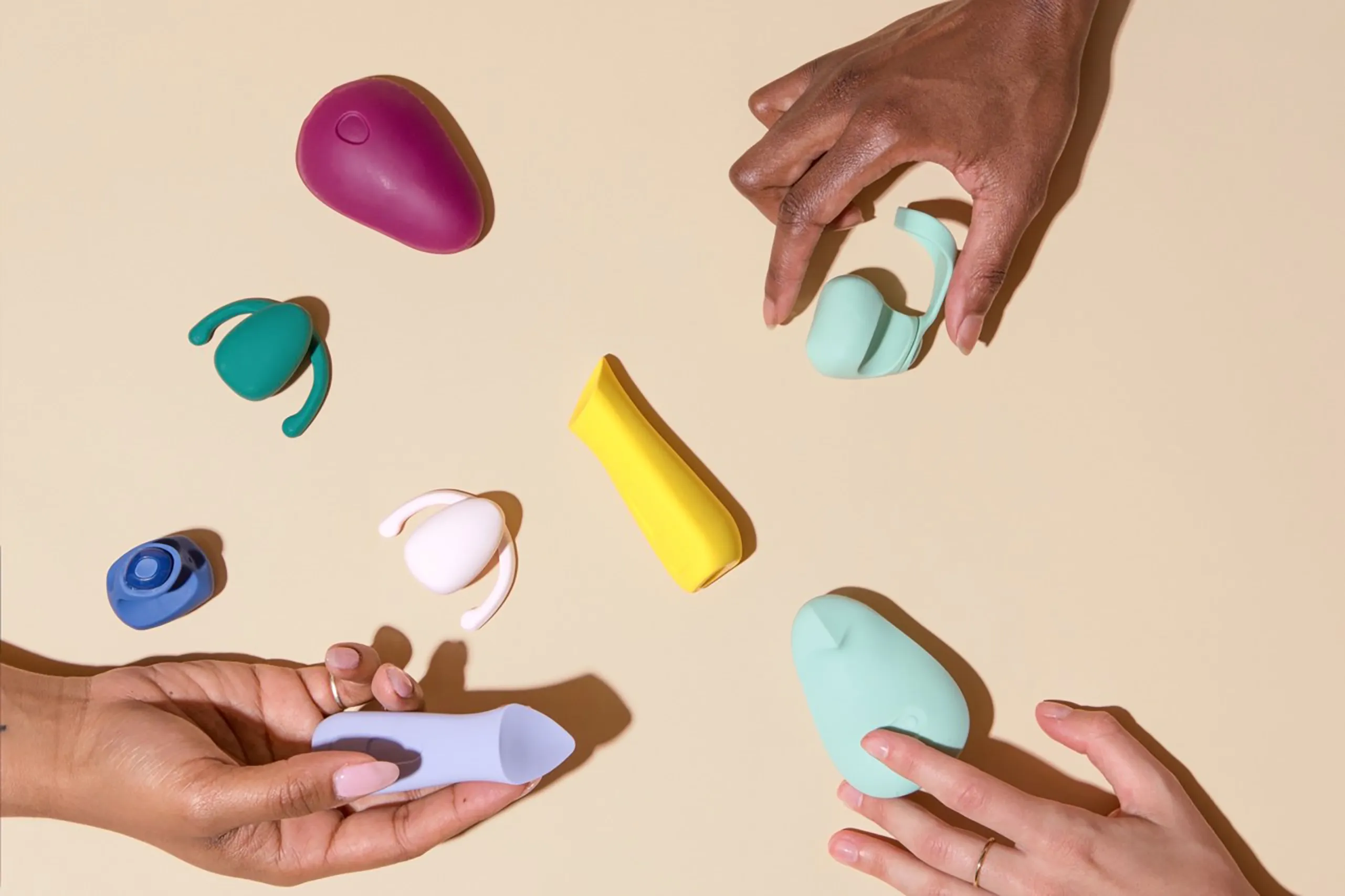 Hands interacting with colorful Dame sexual wellness devices on a beige background