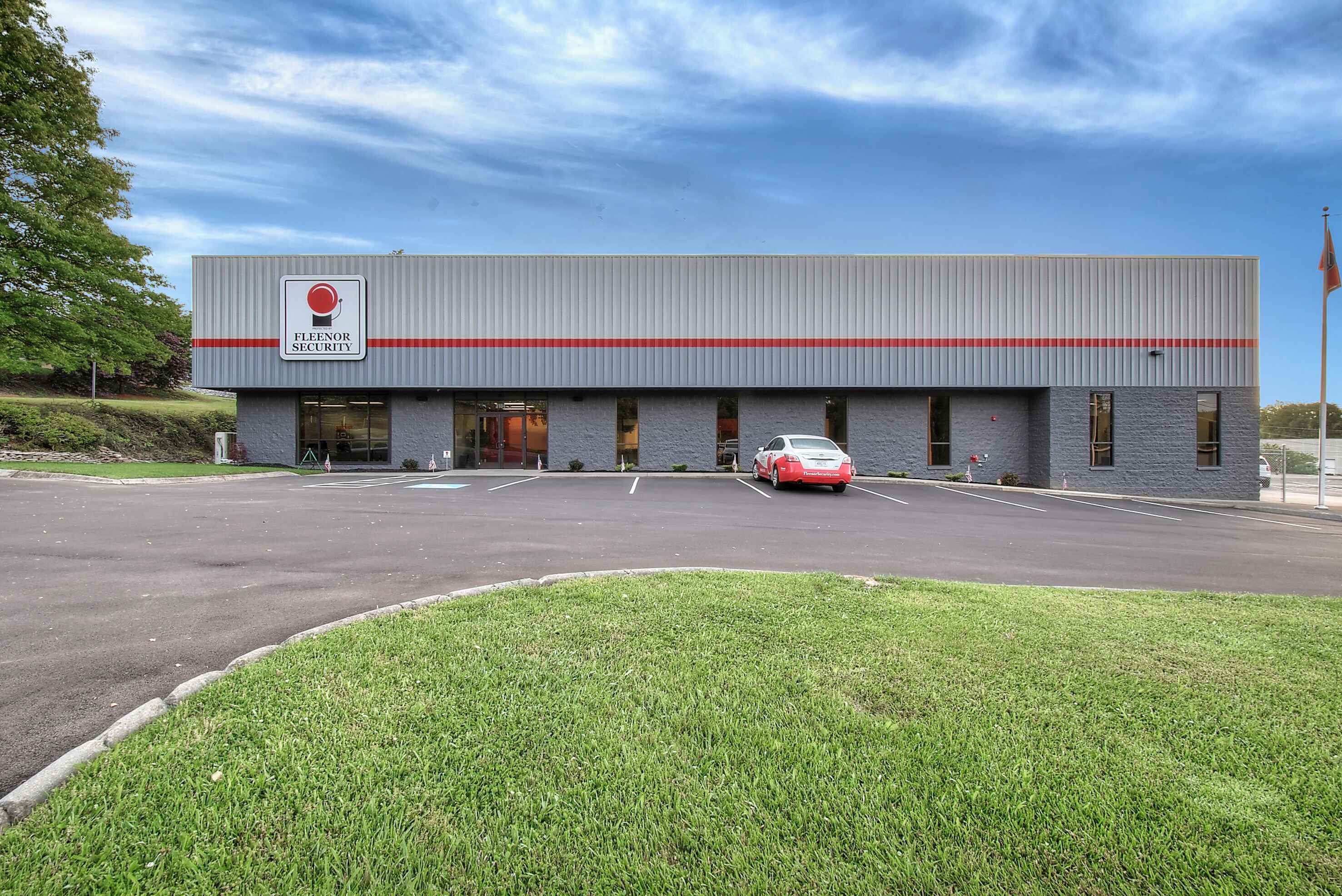 A modern commercial building with large windows, grassy area in front, and a cloudy blue sky above.