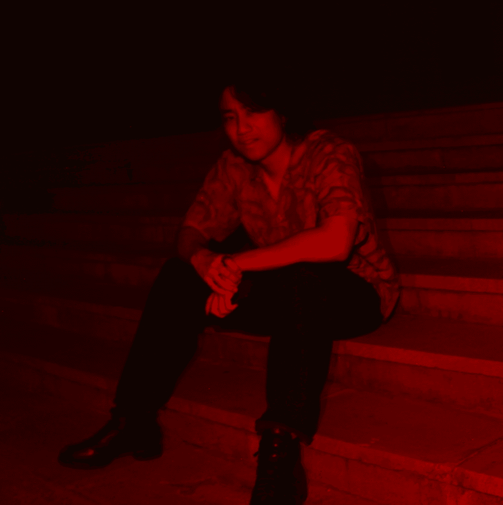 black and red image of man looking at camera while sitting on steps