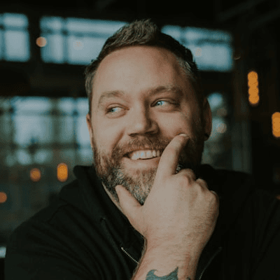 Hombre con barba mirando a ala derecha con sonrisa y tatuaje en el brazo