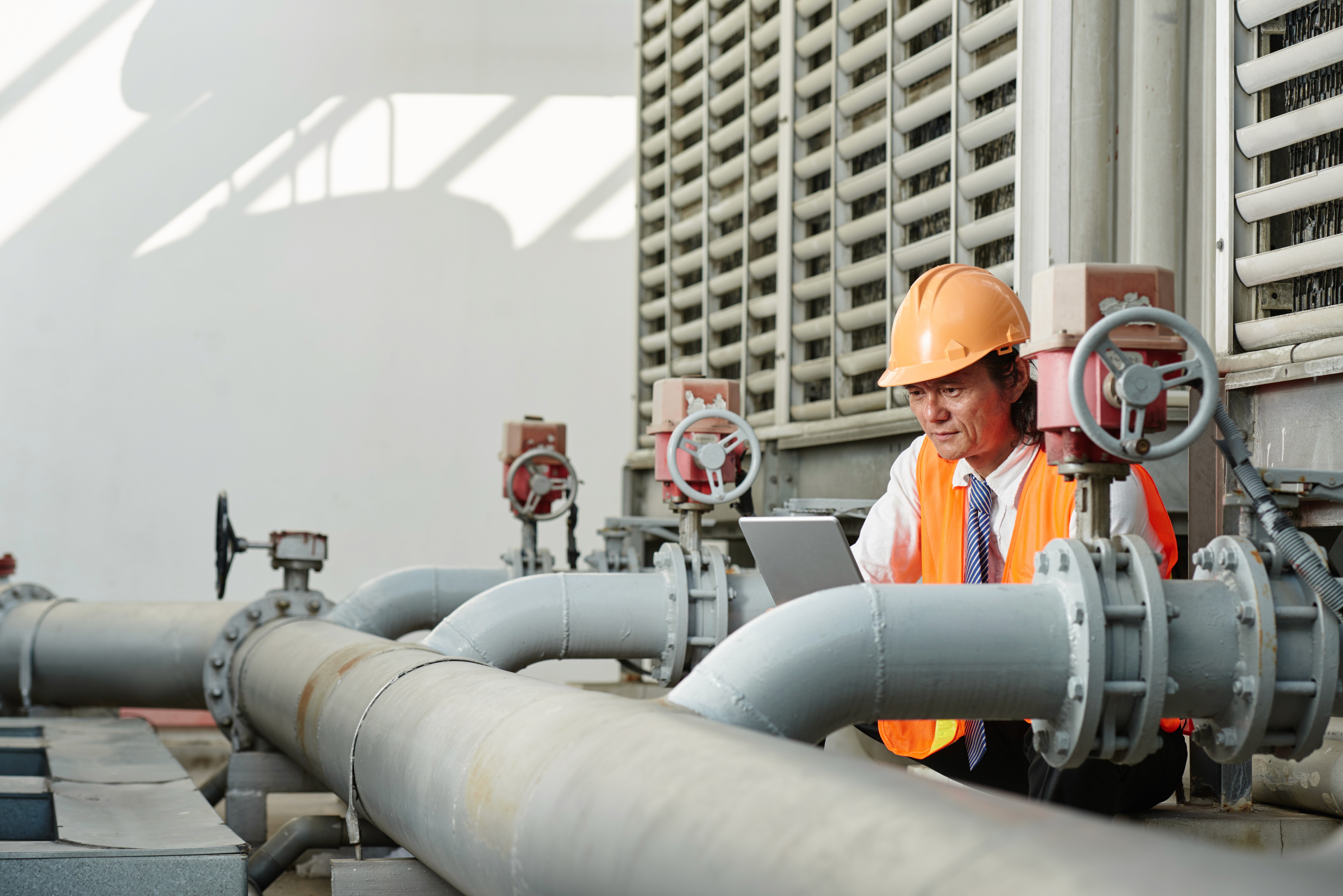 Man wearing protective gear checking pumps and valves in the oilfield equipment.