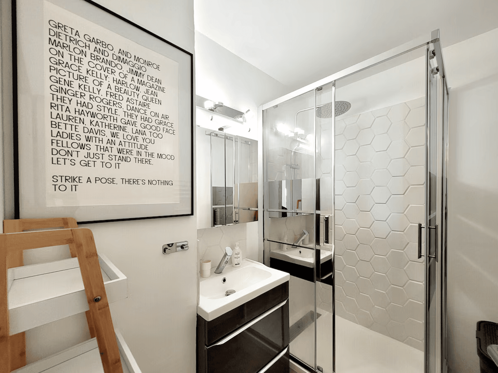 A modern bedroom features a cozy bed with white pillows, a striped rug, and a stone wall with a fireplace. Art with blue stones adds flair, while soft light creates a serene atmosphere.