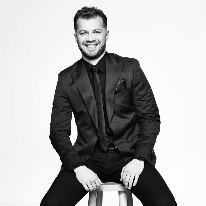 A young man in a white t-shirt stands against a light-colored background.