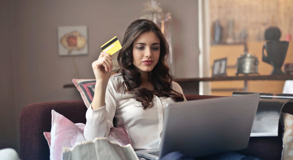 Woman shopping online with credit card, using laptop on sofa in cozy home setting.