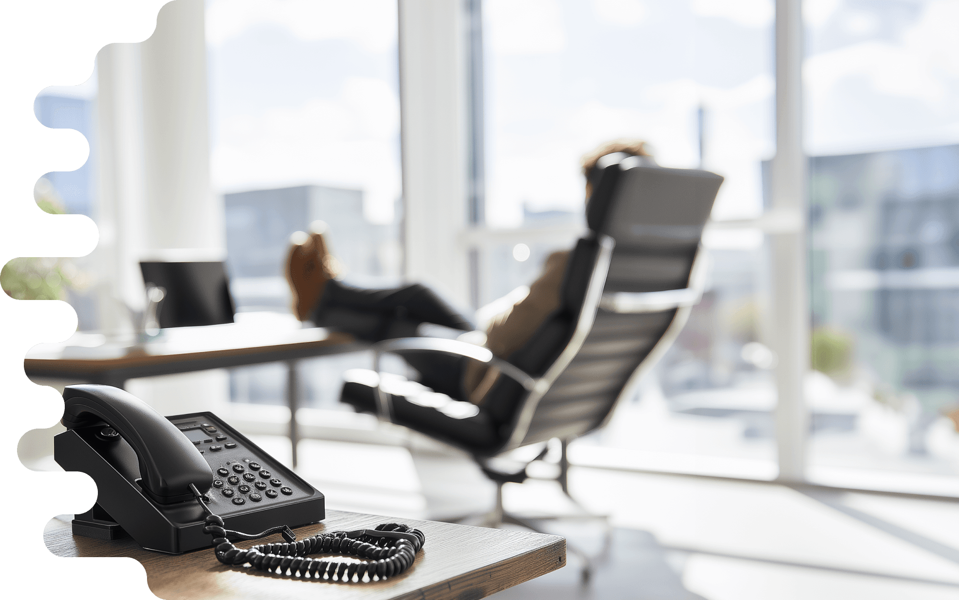 Bürotelefon im Vordergrund auf einem Schreibtisch, im unscharfen Hintergrund sitzt eine Person in einem Bürostuhl vor einem Fenster mit Stadtblick. Eine Zimmerpflanze in einem Topf steht links im Bild. Die Szene ist in warmen Morgenlicht getaucht und vermittelt eine ruhige, professionelle Arbeitsatmosphäre."