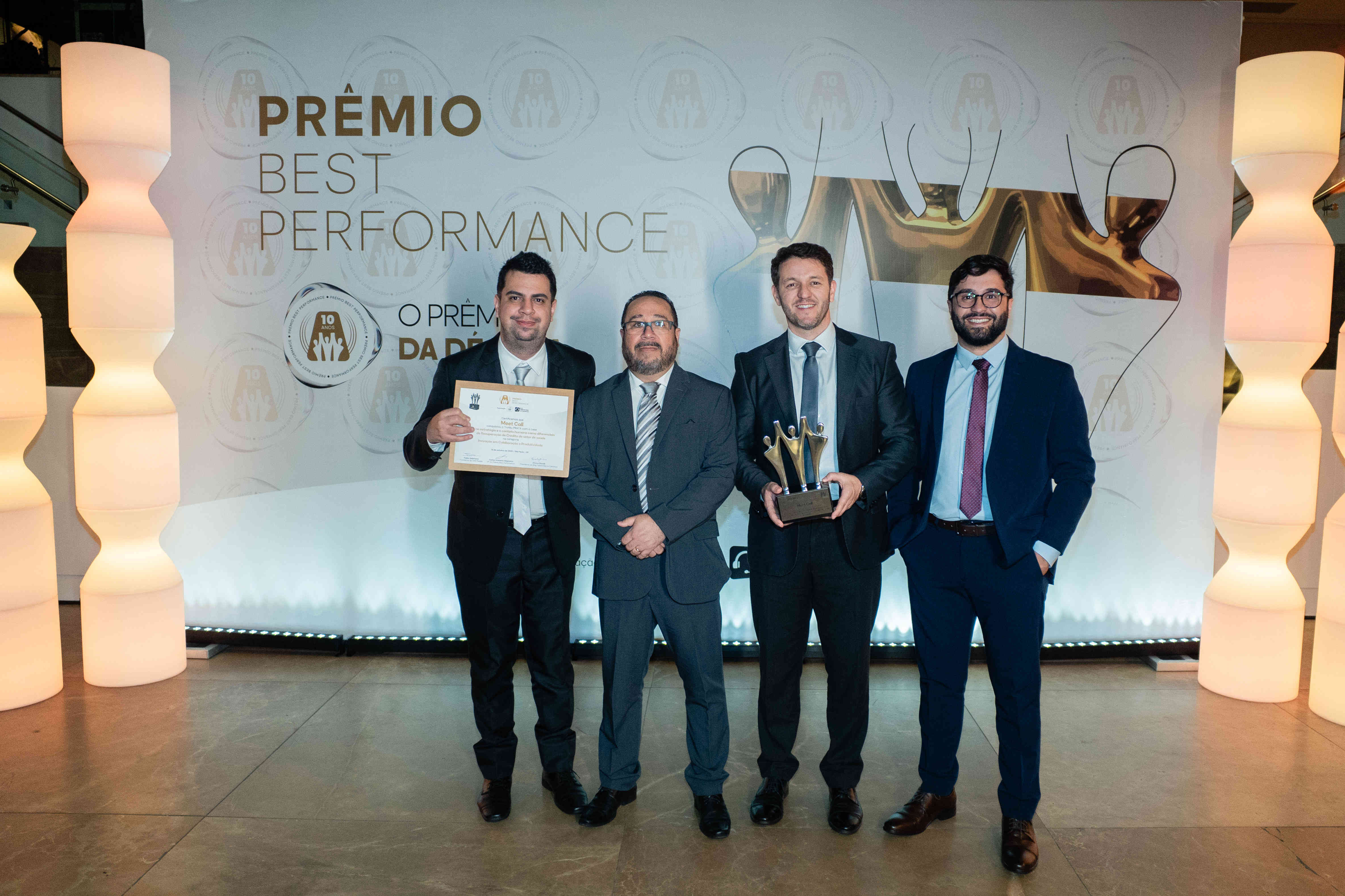 Executivos da Meet Call posando com troféu prata e certificado no palco do Prêmio Best Performance 2025