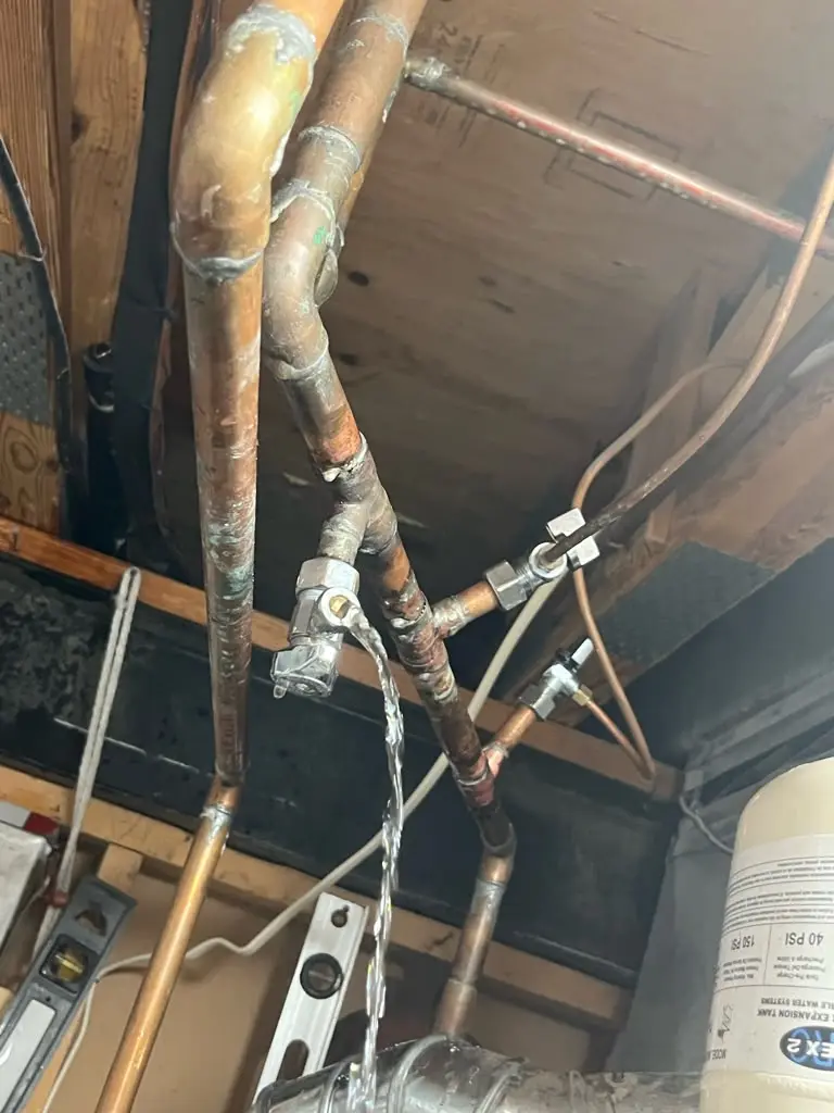 Water spraying aggressively from a broken copper pipe valve, requiring immediate emergency water leak repair.