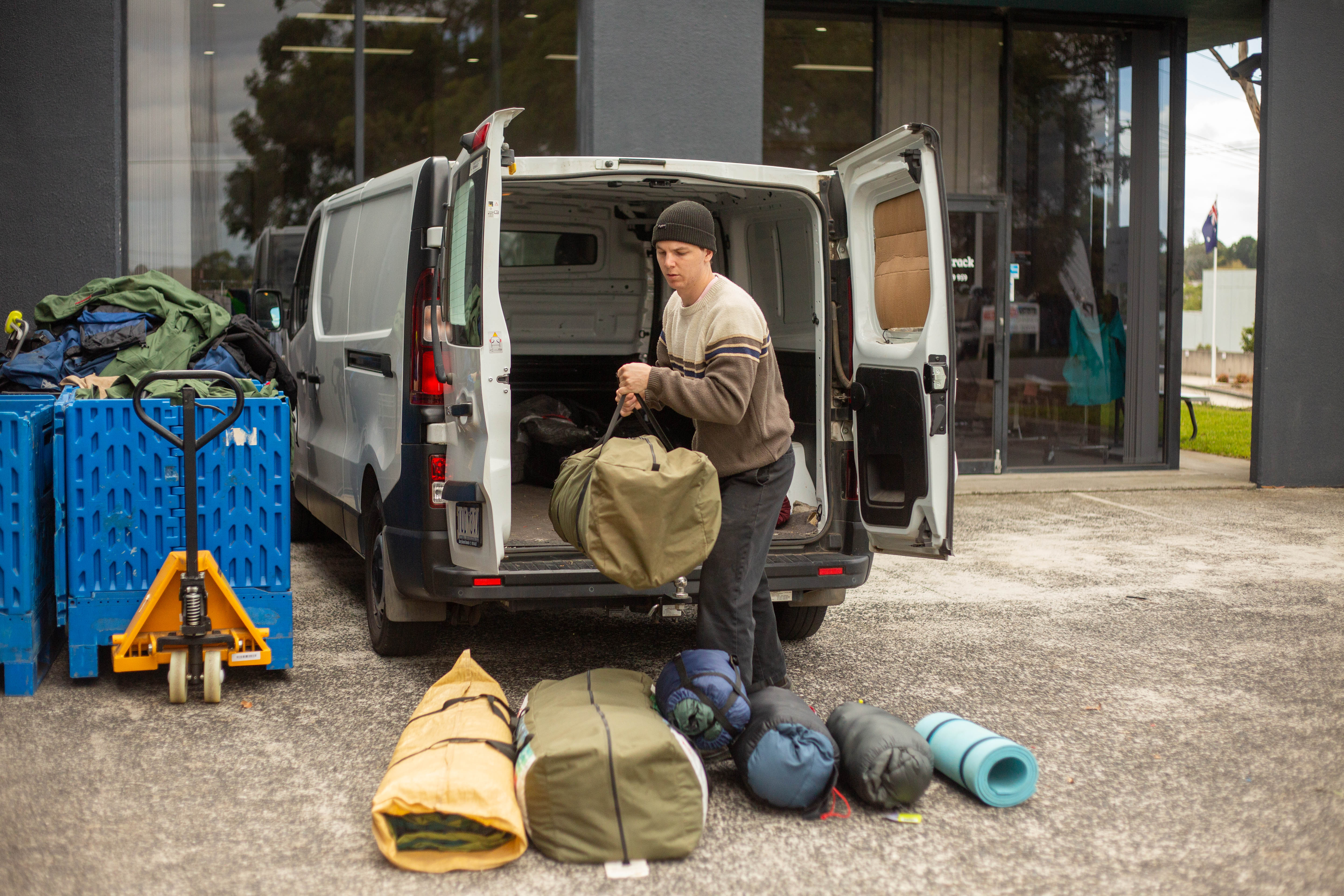Person unloading sleeping bags and tents from a van, preparing discarded outdoor gear for upcycling.