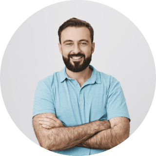 A man with a beard wearing a blue shirt, standing confidently with a neutral expression.