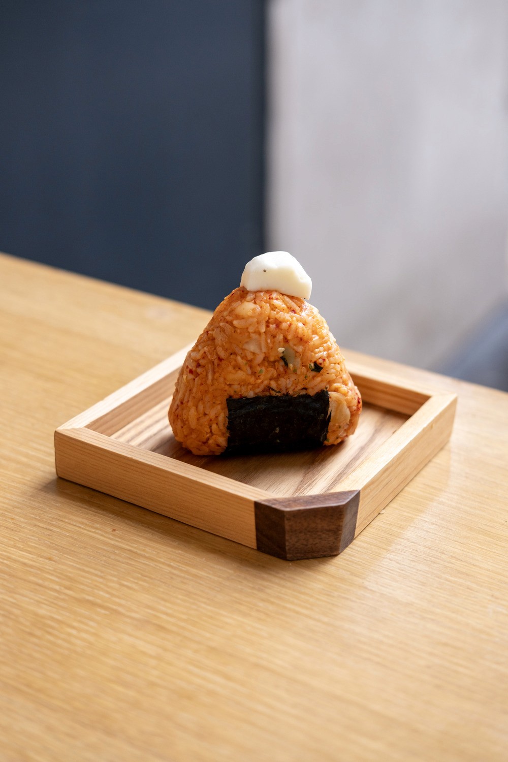 White plate with roasted carrots served on green sauce, topped with almonds and fresh herbs, held by a hand over a dark table.