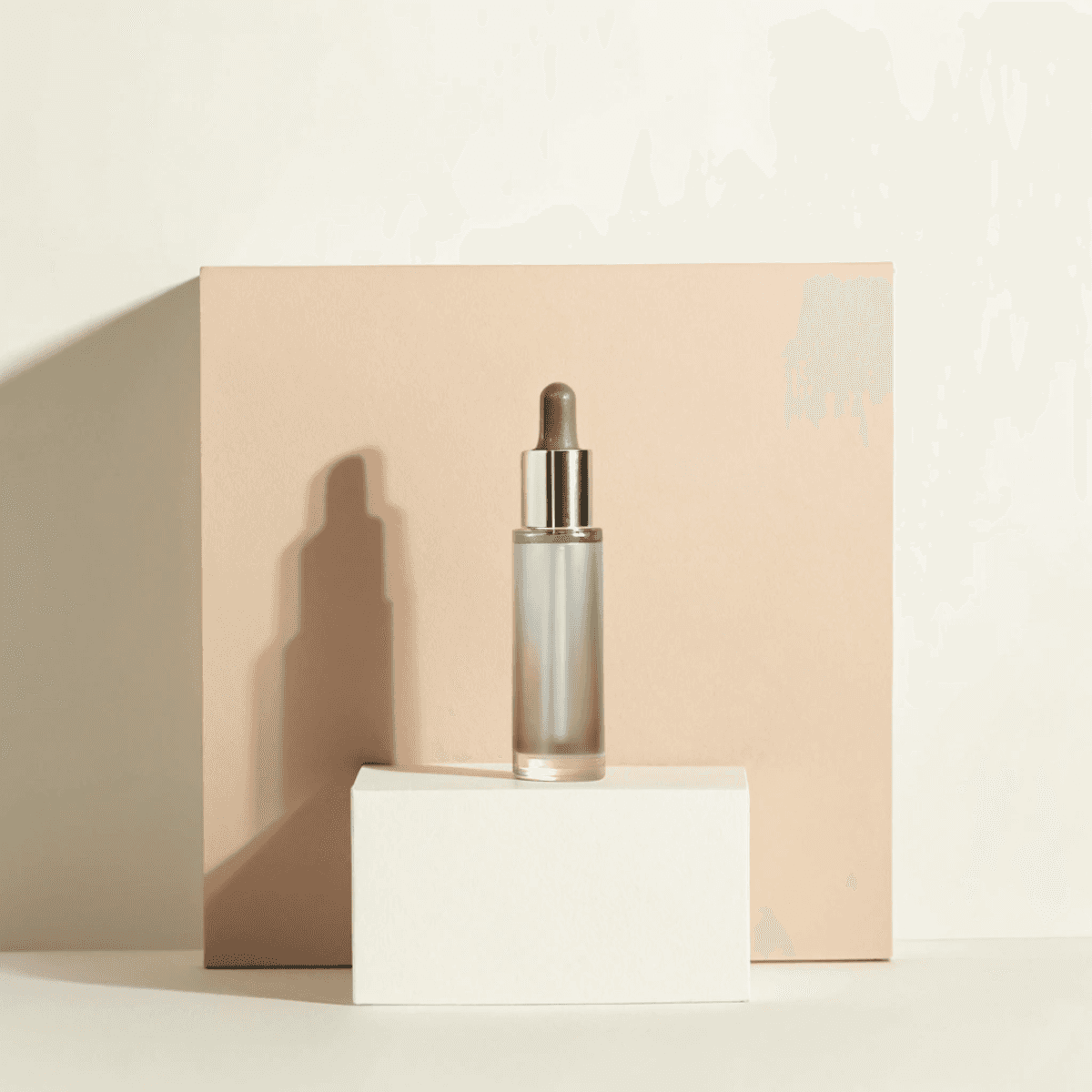 A minimalist skincare bottle with a dropper lid is elegantly displayed against a soft beige background and a white rectangular block, highlighting its luxury branding.