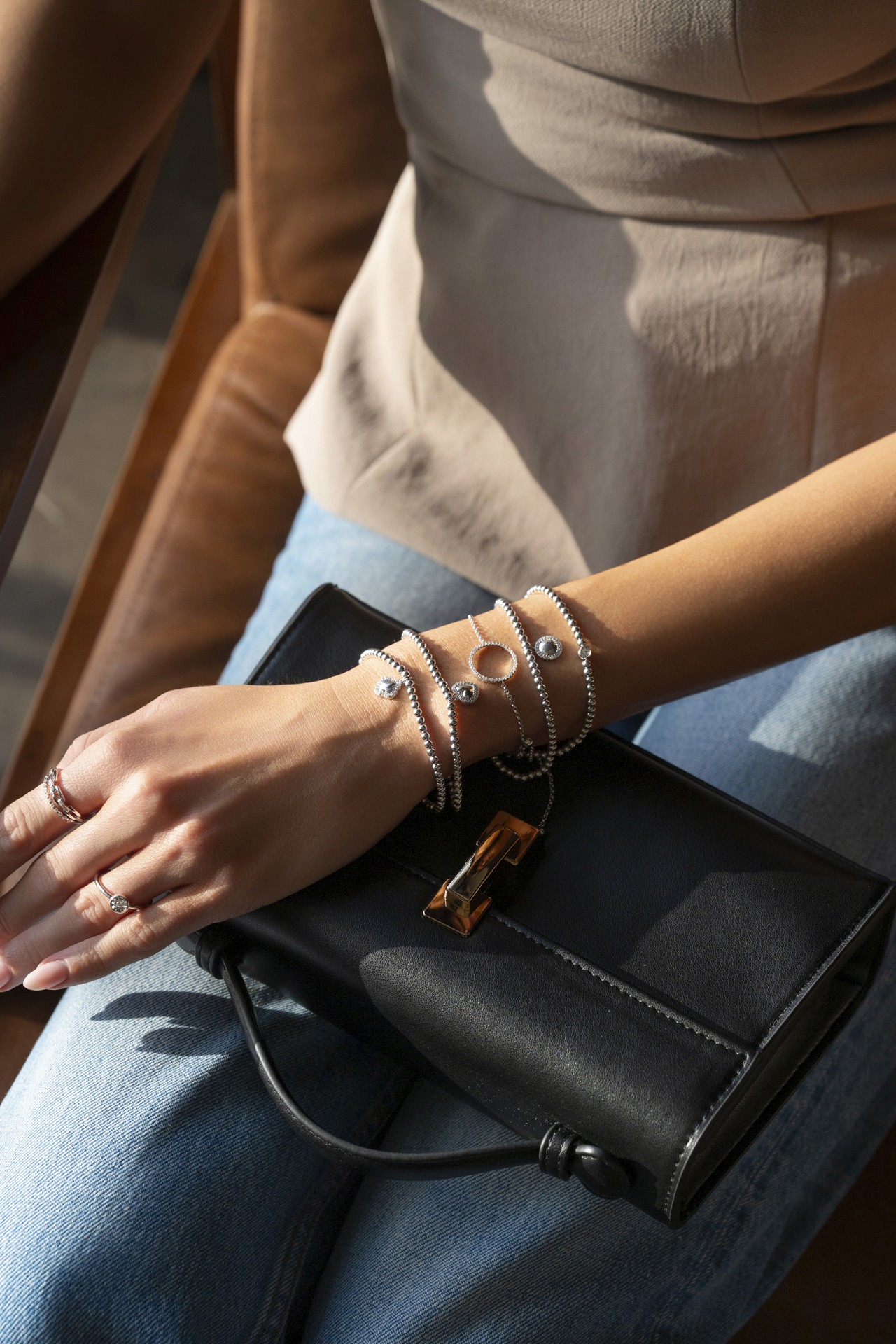 group of bracelets photographed in a fashion editorial style, showcased in contrast to a black purse, and a model wearing a beige top and jeans.