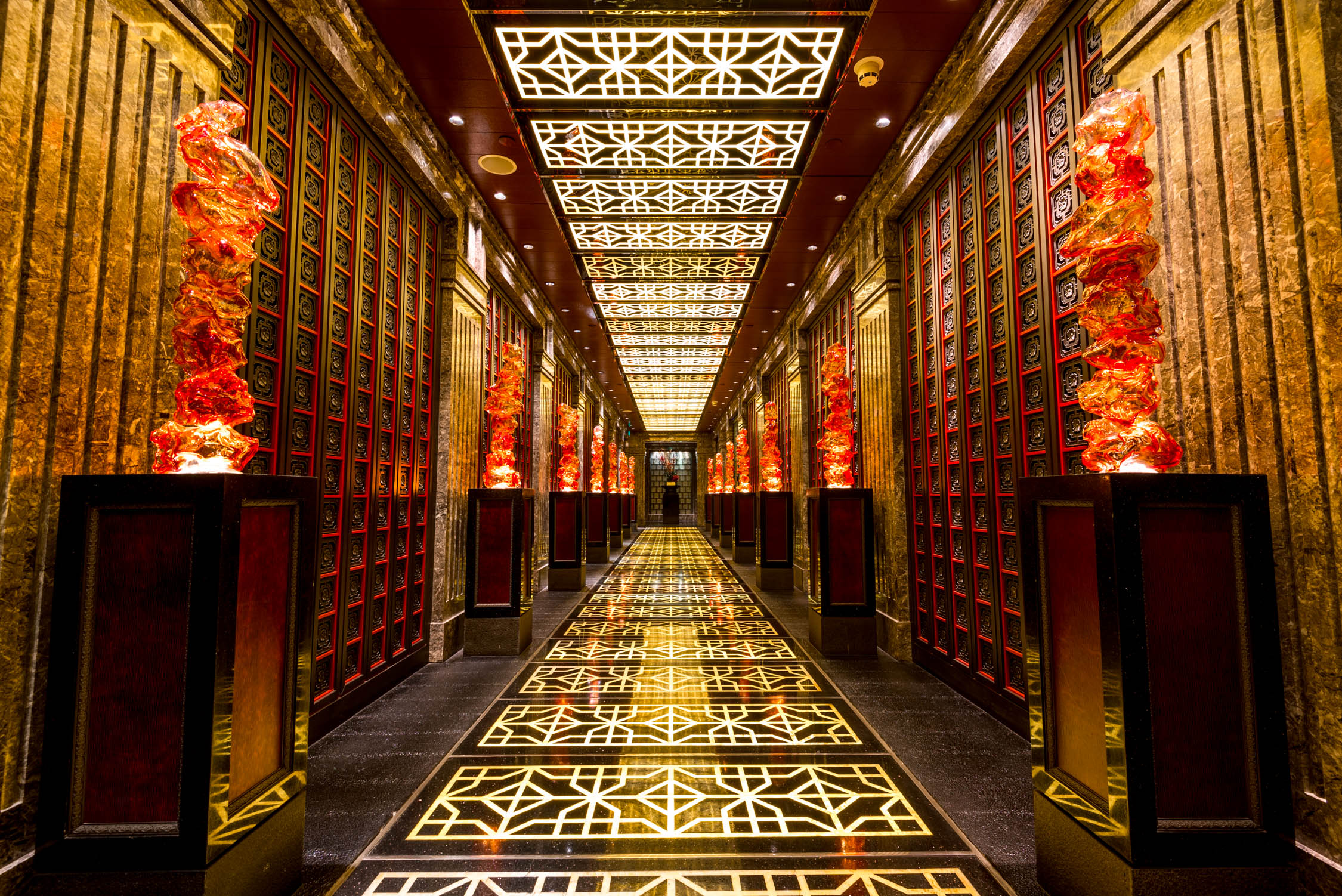 A long hallway features ornate gold and red patterned ceilings, decorative wall panels, and tall floor lanterns with orange