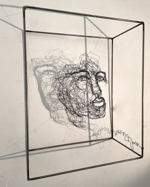 Sculpture en fil de fer représentant le visage d'une femme dans un cadre en fil de fer, vue détaillée de côté avec son ombre projeté sur le mur