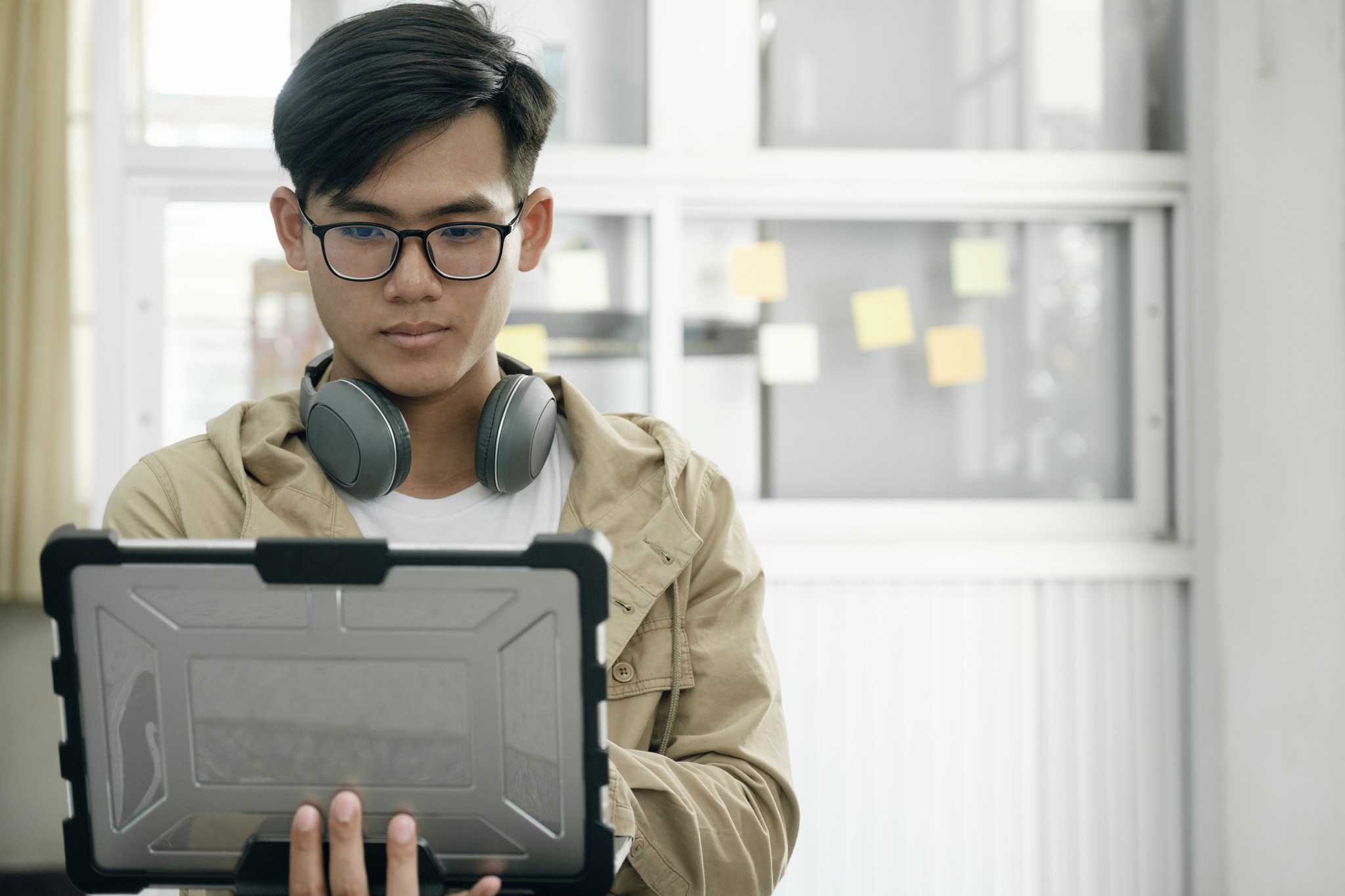 A young man with headphones and glasses holds a tablet, ready to engage with new telecom technologies and innovations.