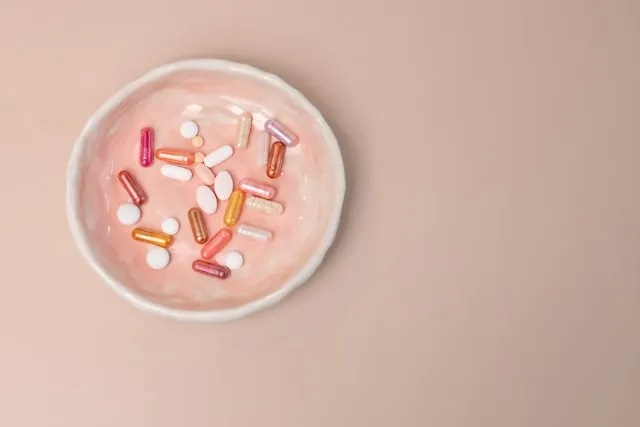 Colorful capsules and tablets in a small pink bowl