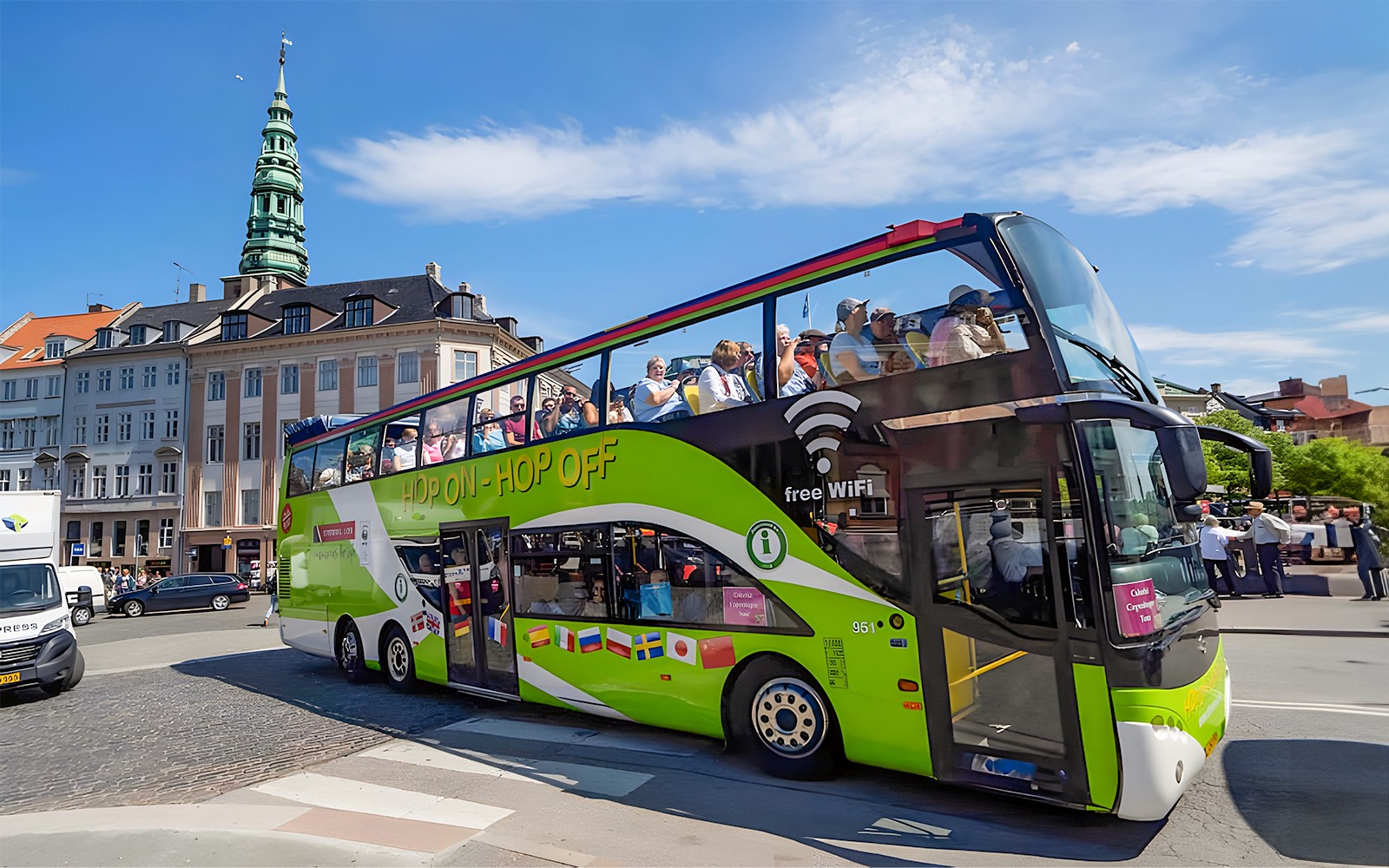 Hop-on hop-off busz Koppenhágában turistákkal, történelmi épületek és torony közelében.