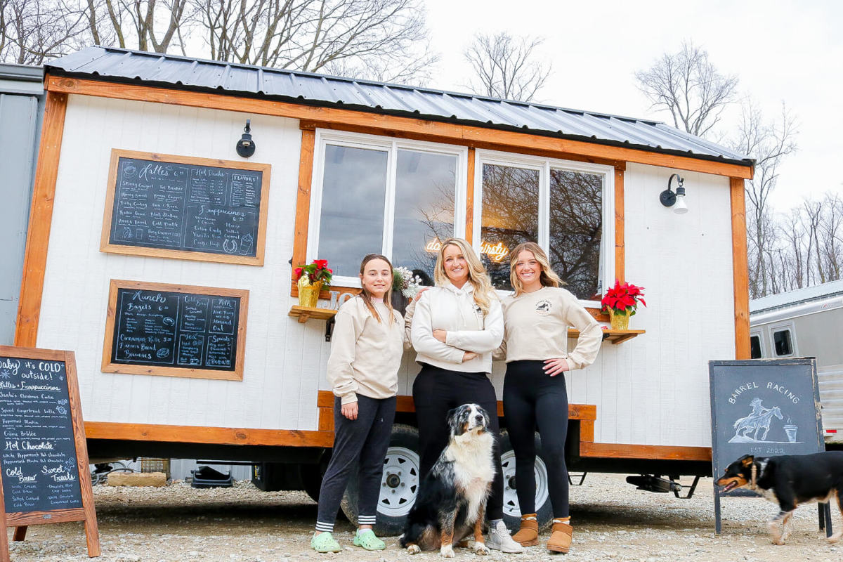 A tall stack of French toast or waffles, heavily drizzled with syrup and topped with slices of banana, dusted with powdered sugar, and served in dramatic, dark lighting.