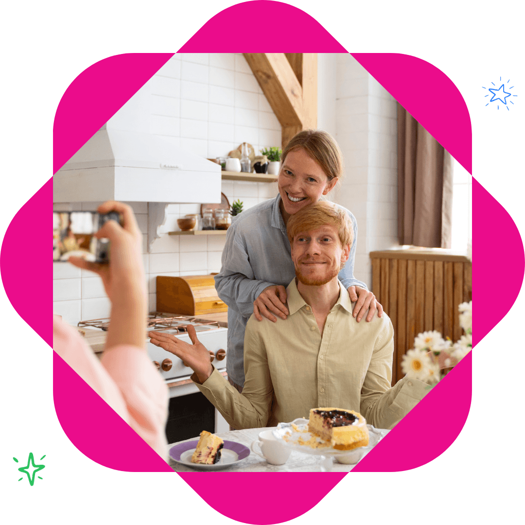 Couple taking a photo of cake in the kitchen, smiling and looking at the camera with food on the table.