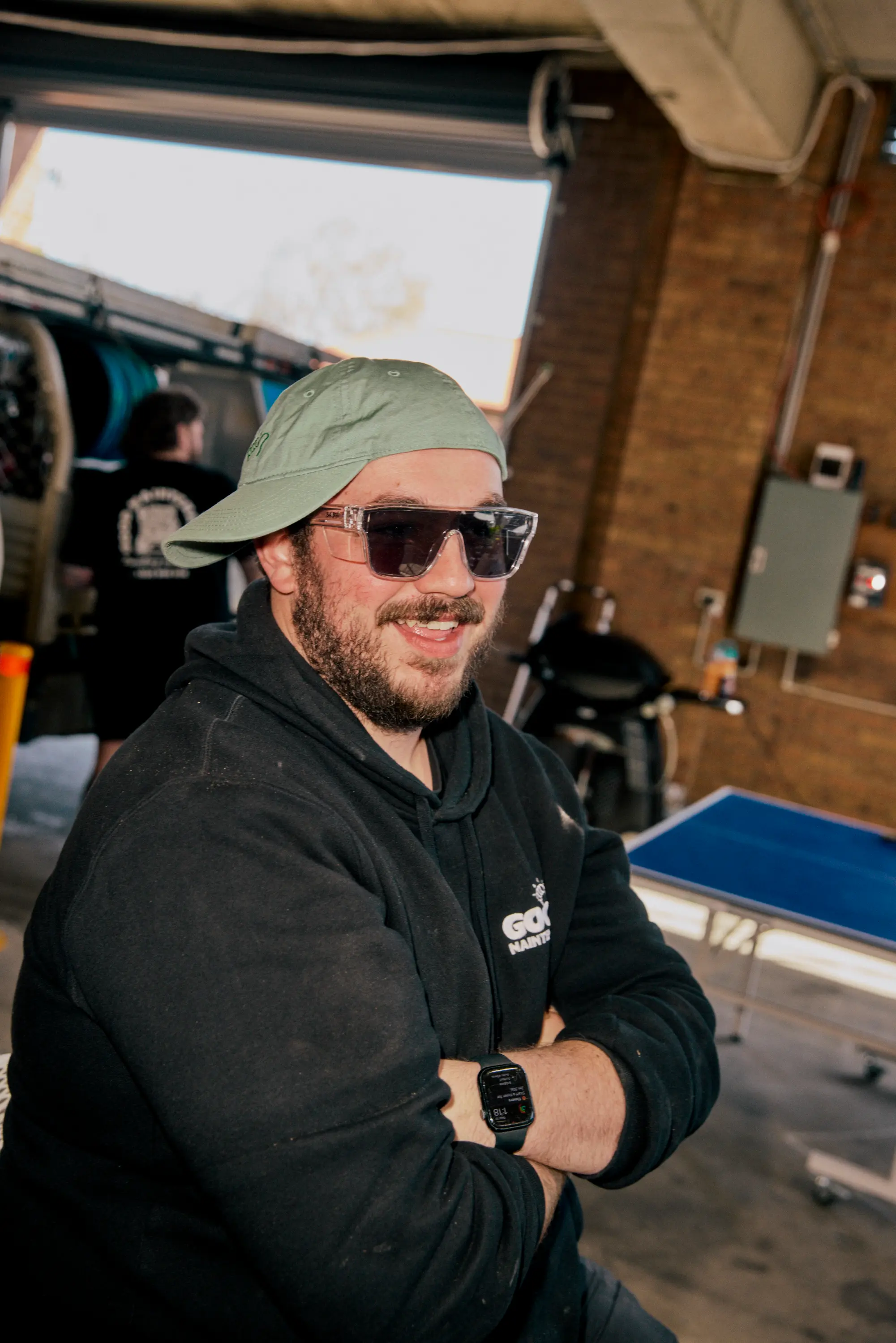 Team Member in Good Maintenance hoodie and sideways cap, smiling.