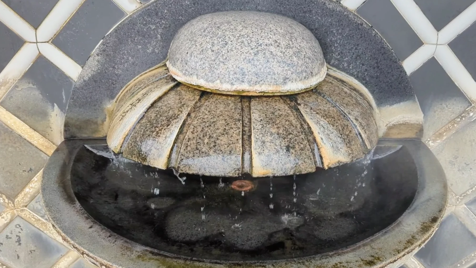 Hot spring water spilling from a stone spout into a shallow drinking basin.