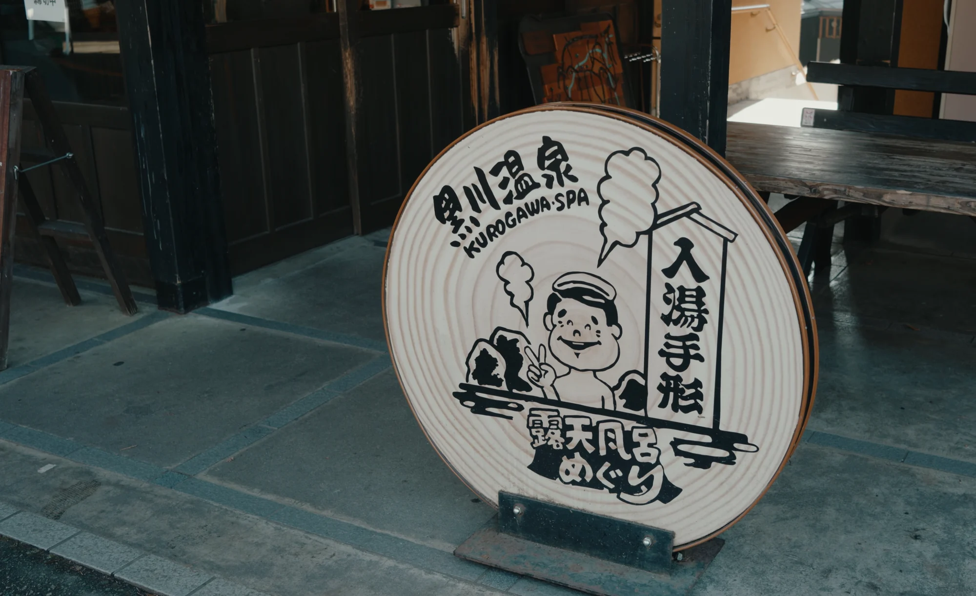 A large circular wooden sign shaped like a tegata bath pass outside a timber building