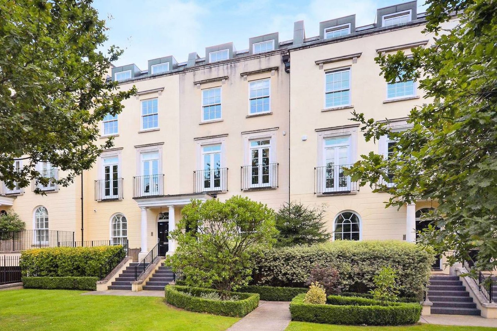 A smiling man with curly hair is sitting at a desk, looking at the camera, with a laptop and a lamp in the background.