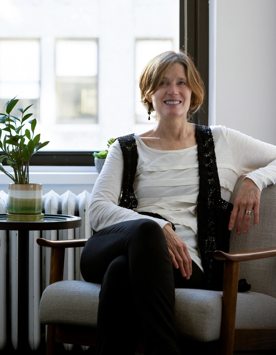 photo of a expansive therapy therapist sitting relaxed in a chair in front of new york city view representing safety and inclusivity found through LGBTQ group therapy