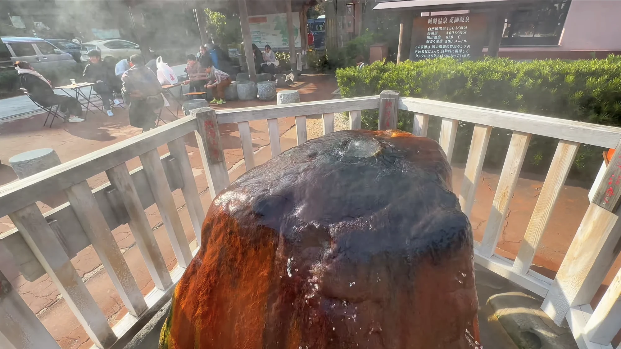 A steaming mineral-crusted spring vent behind a wooden fence at the Kinosaki source.