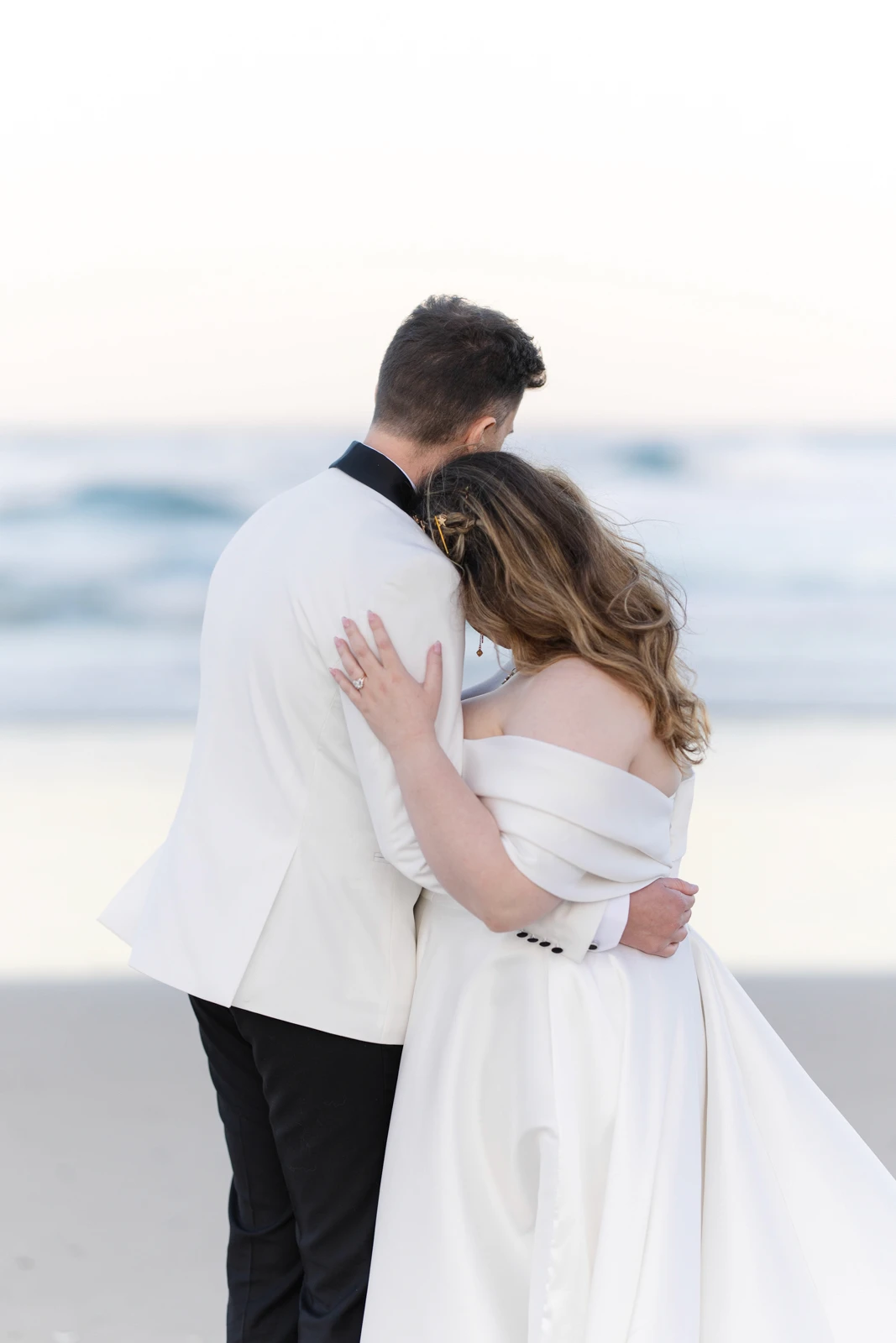 Bride and groom resting their heads together looking at the ocean