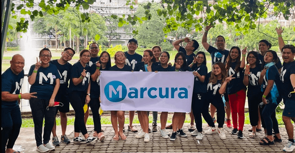 A group of people in matching shirts poses together outdoors, holding a banner with the logo for "Cartera."