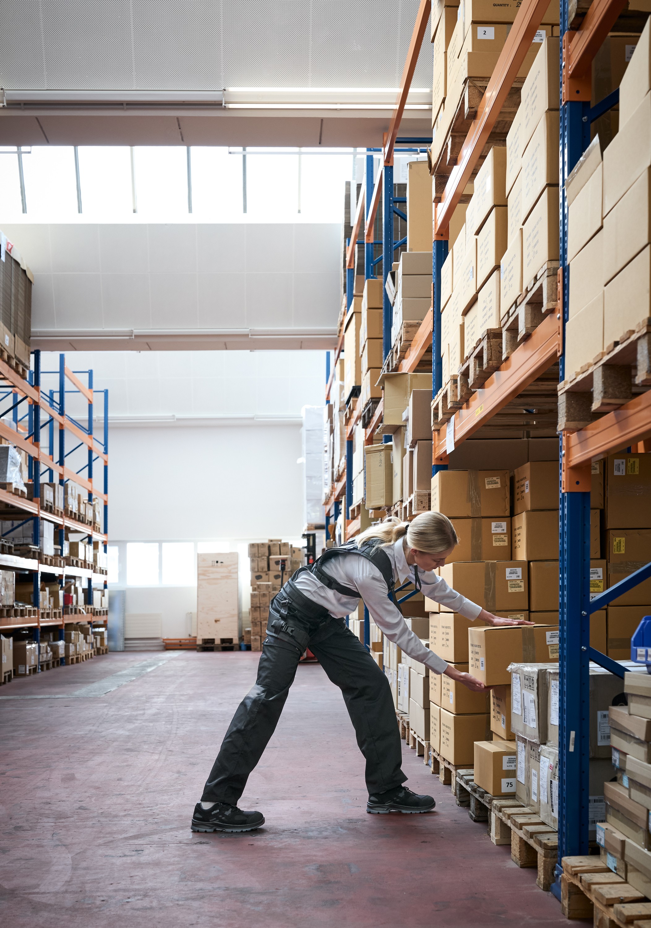 Warehouse worker lifting a box while wearing a LiftSuit exoskeleton, providing back support.