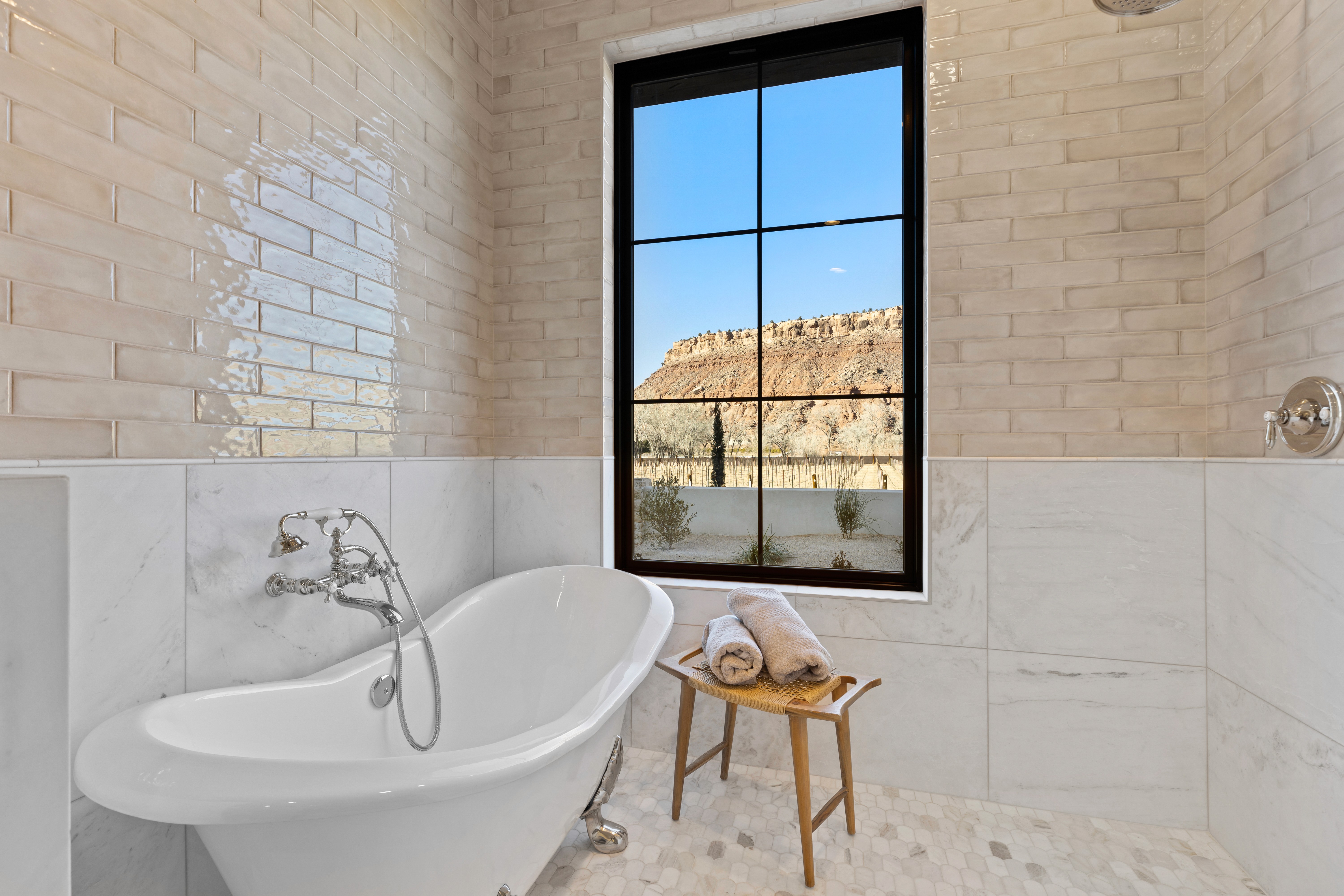 Walk-in shower with a freestanding tub, chrome and polished nickle plumbing fixtures in a full tiled shower and a large, gridded window.