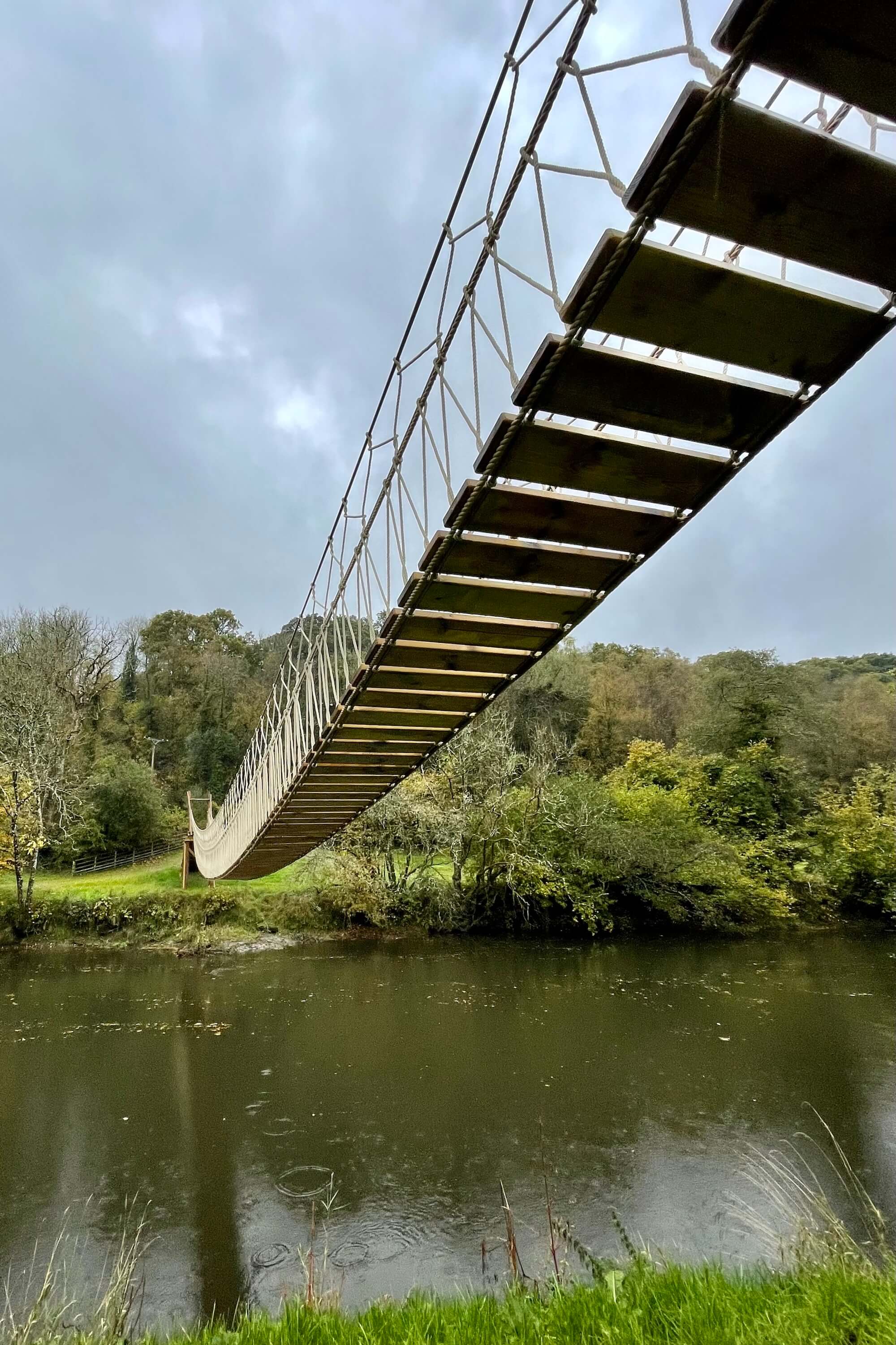 Long suspension bridge carrying pipelines over blue water towards industrial buildings.