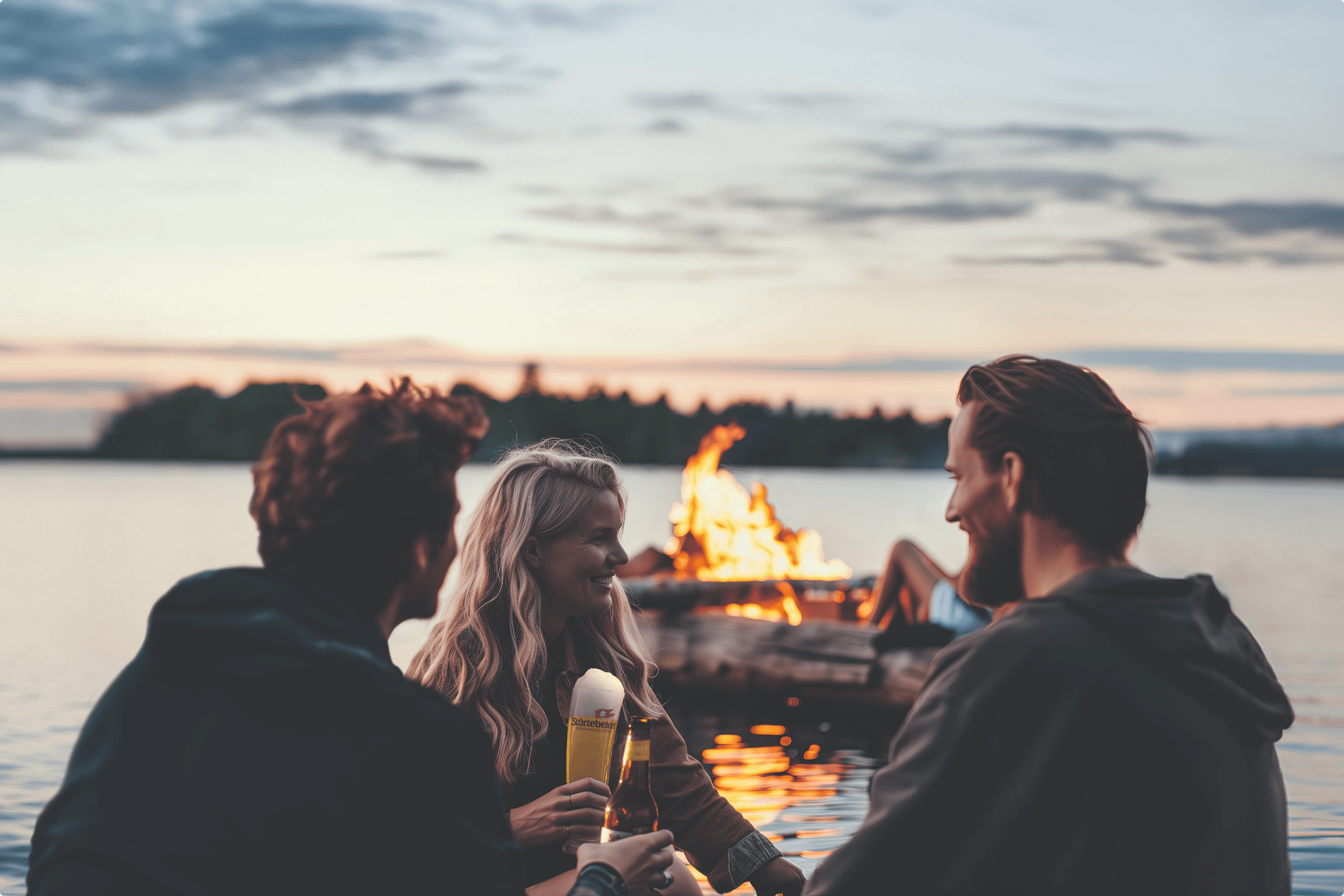 Friends by a campfire with drinks at sunset