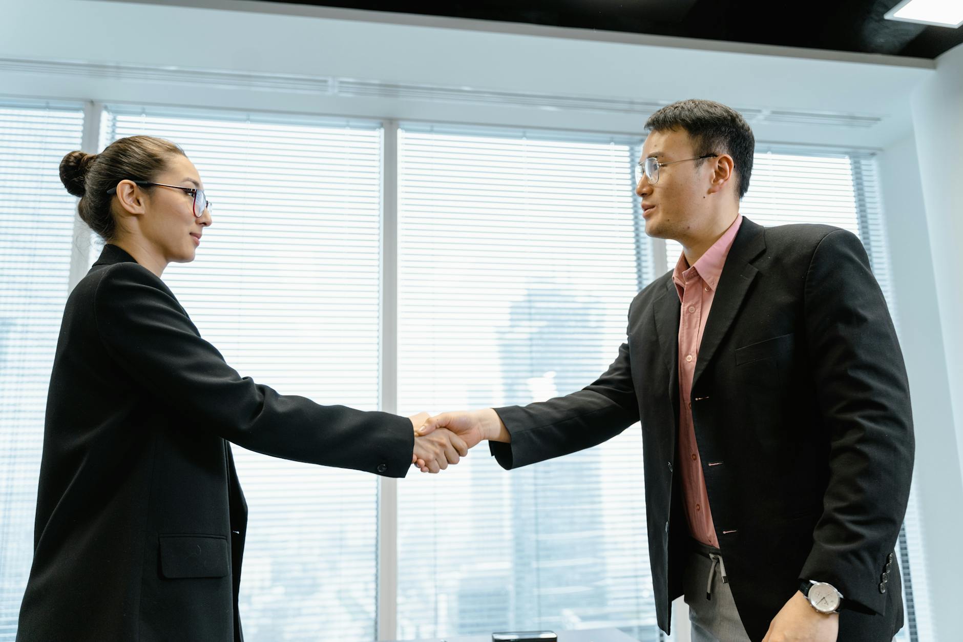 Two colleagues shaking hands at an education conference with blurred networking crowds in the background.