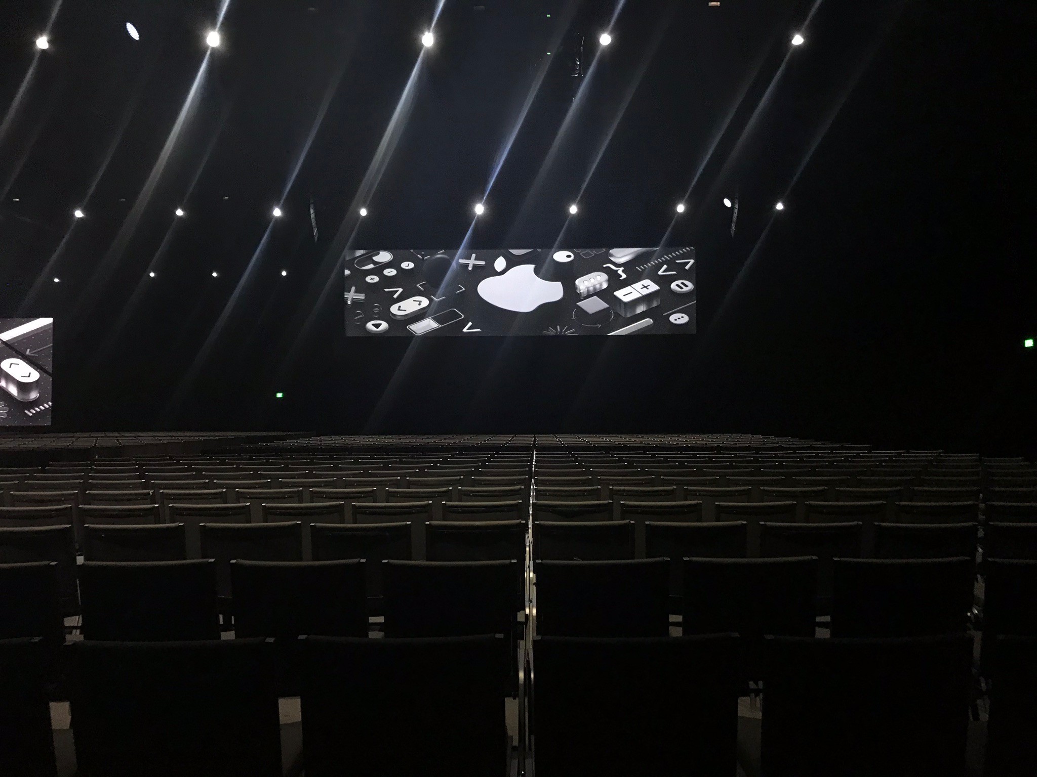 Dark auditorium with rows of seats facing a stage screen, capturing the scale of a large Apple event setup.