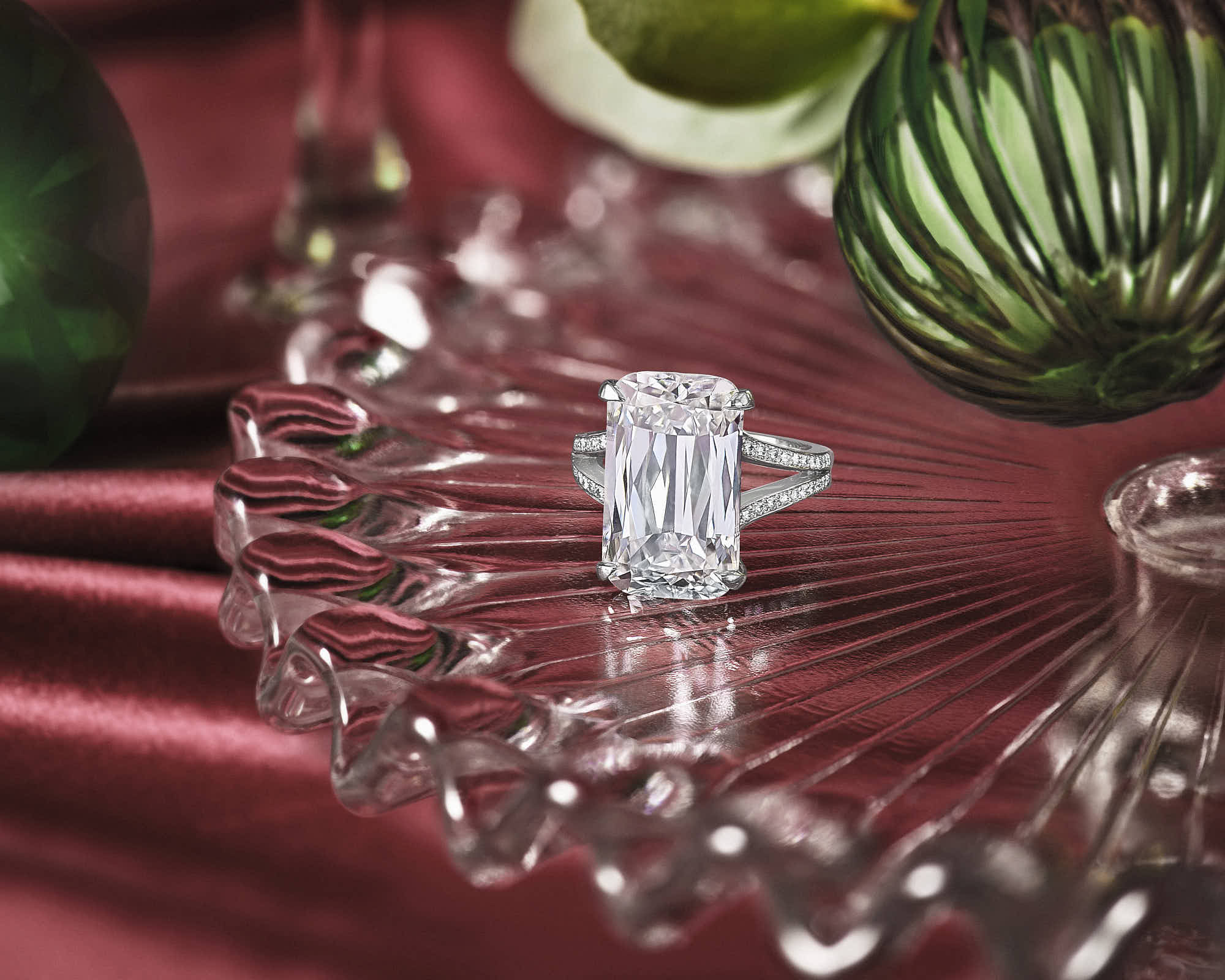 Elegant emerald-cut diamond engagement ring on glass platter with luxurious red satin background.