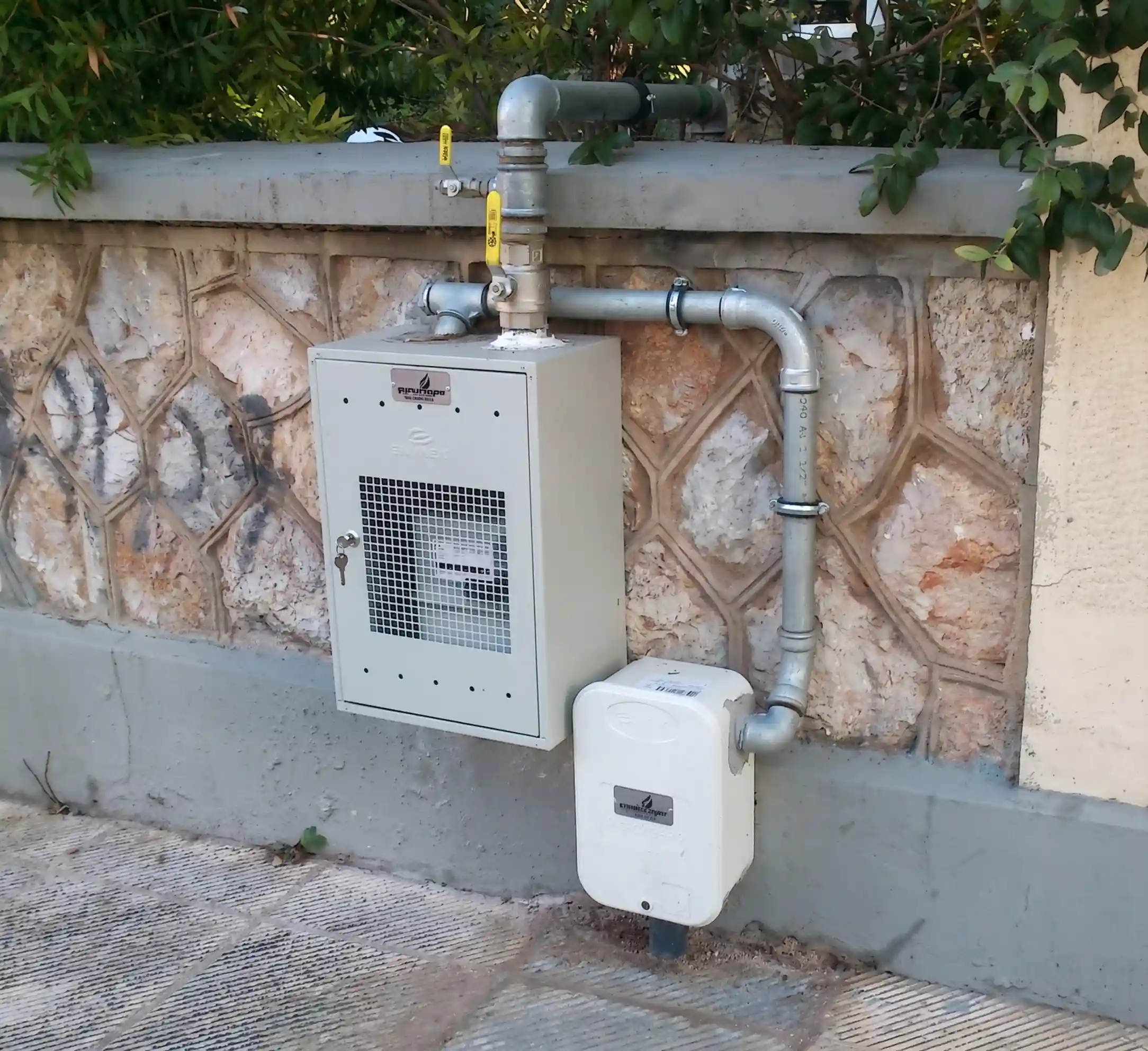 Εξωτερικός μετρητής φυσικού αερίου σε ερμάριο με σωληνώσεις σε πέτρινο τοίχο.